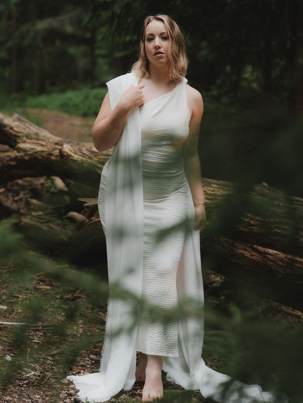 Ethereal white dress portrait in moody forest setting with dappled sunlight creating dramatic shadows.