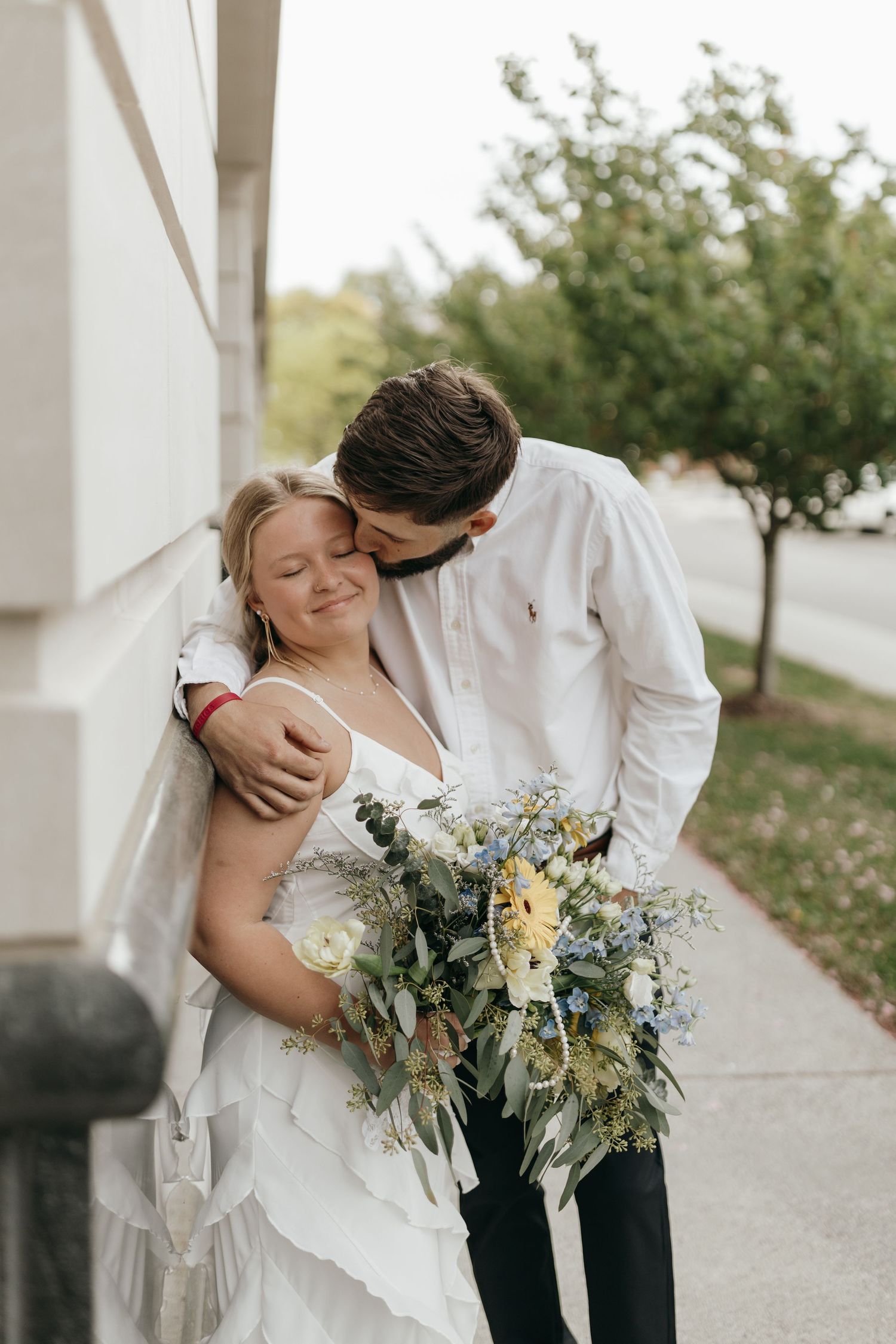 A romantic wedding moment captured outdoors with a beautiful bouquet of mixed flowers and greenery.