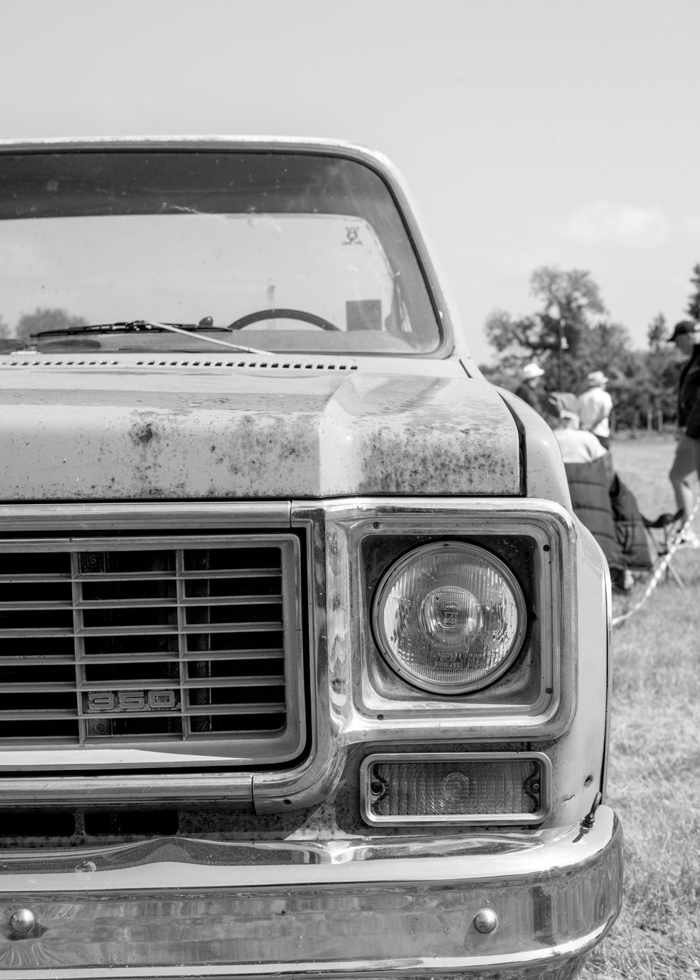 Black and white photo of vintage Chevrolet truck front end showing headlight and grille with weathered patina finish.
