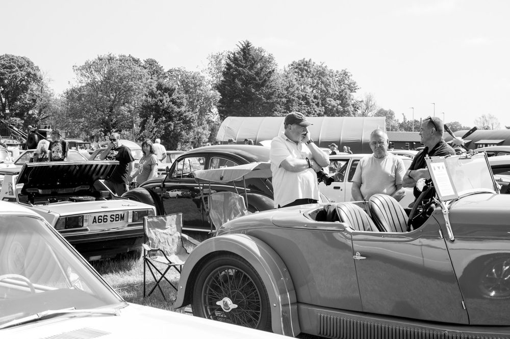 Vintage black and white scene at a classic car show with various automobiles on display.