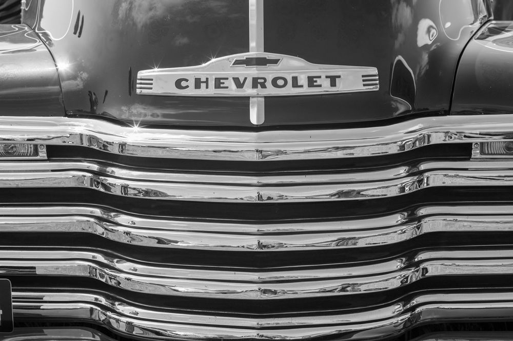 Close-up black and white photograph of a vintage Chevrolet truck's chrome grille with prominent brand lettering.