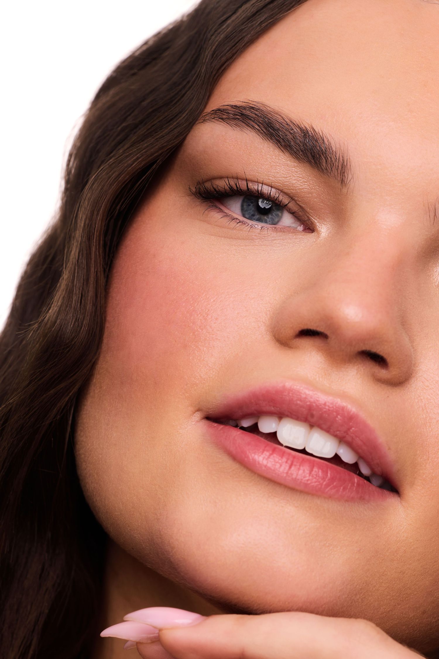 Close-up beauty shot with natural makeup showing glowing skin, pink lips and a gentle smile.