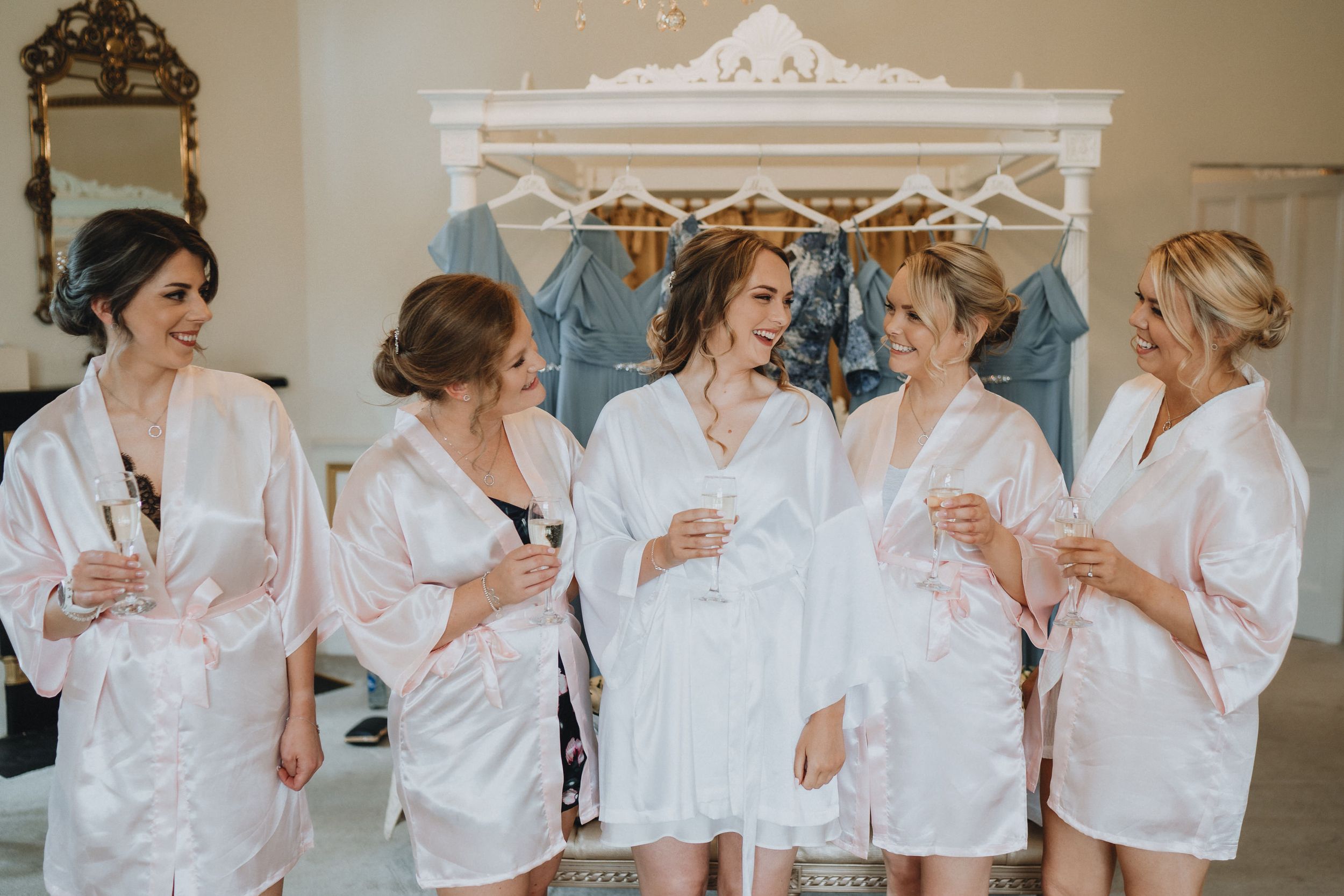 Group wearing matching white robes gather for a celebratory moment during wedding preparation.
