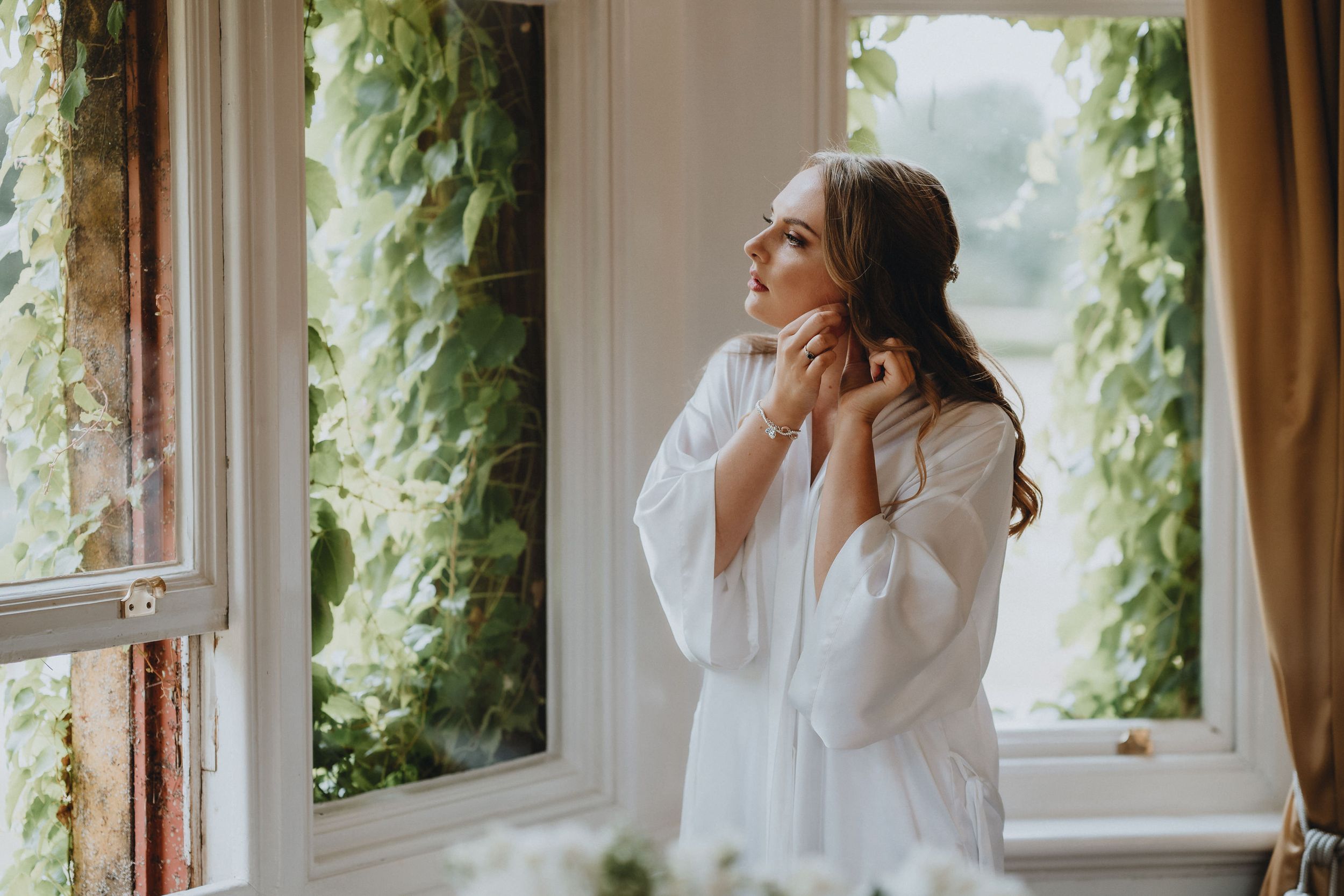 Ethereal morning scene with someone in a white robe by a window framed with lush green vines.