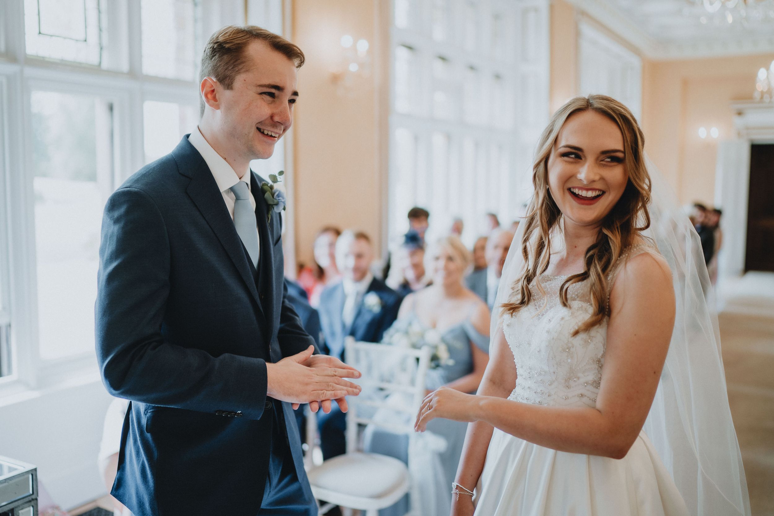 A bride and groom share a joyful moment during their wedding ceremony in an elegant indoor venue.
