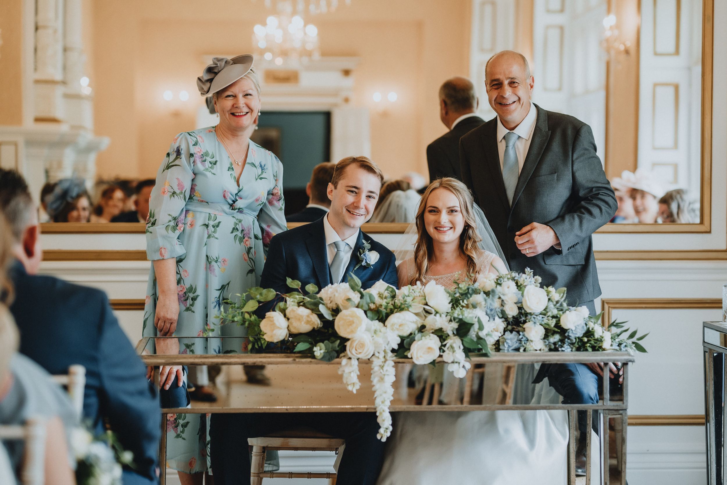 Wedding ceremony participants gather around a decorated table during the marriage signing in an elegant hall.