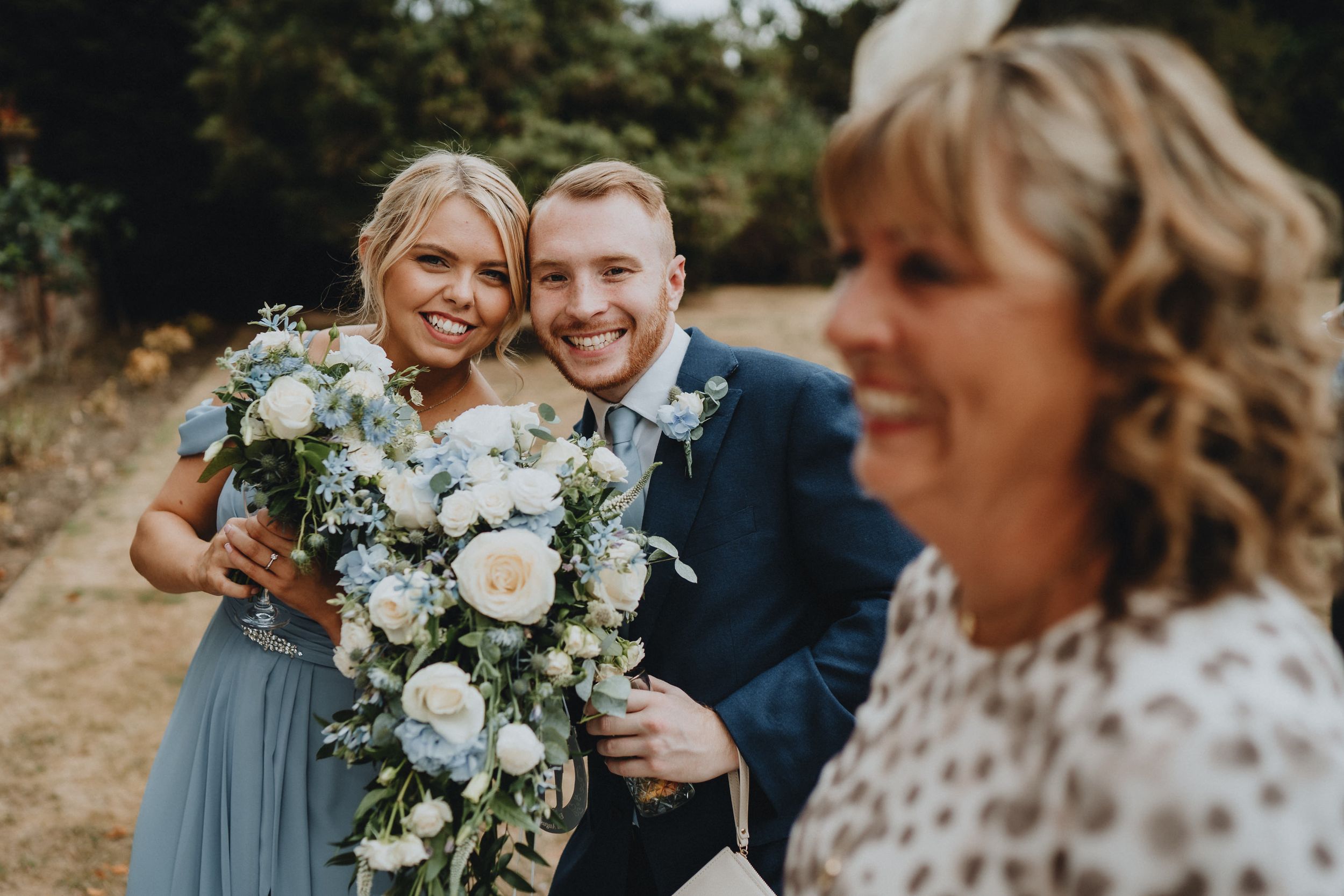 Wedding party members share a candid moment outdoors with elegant white floral bouquet arrangements.