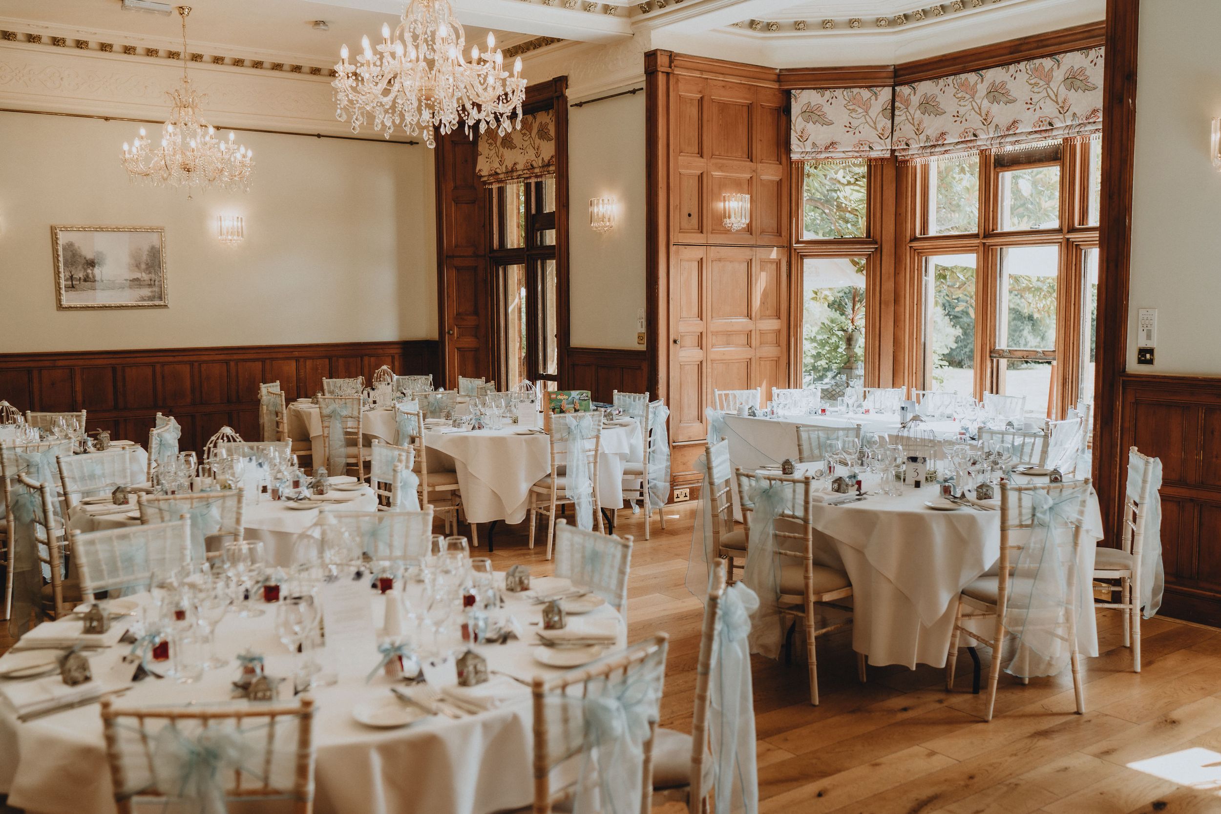 Elegant wedding reception at Holmewood Hall with crystal chandeliers and round tables set with white linens and classic table settings.
