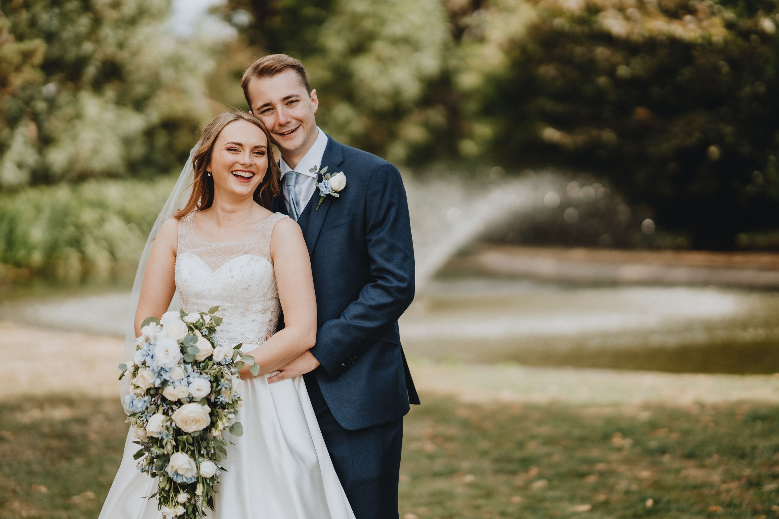 Newlyweds share a joyful moment outdoors with the bride holding a bouquet of white flowers.