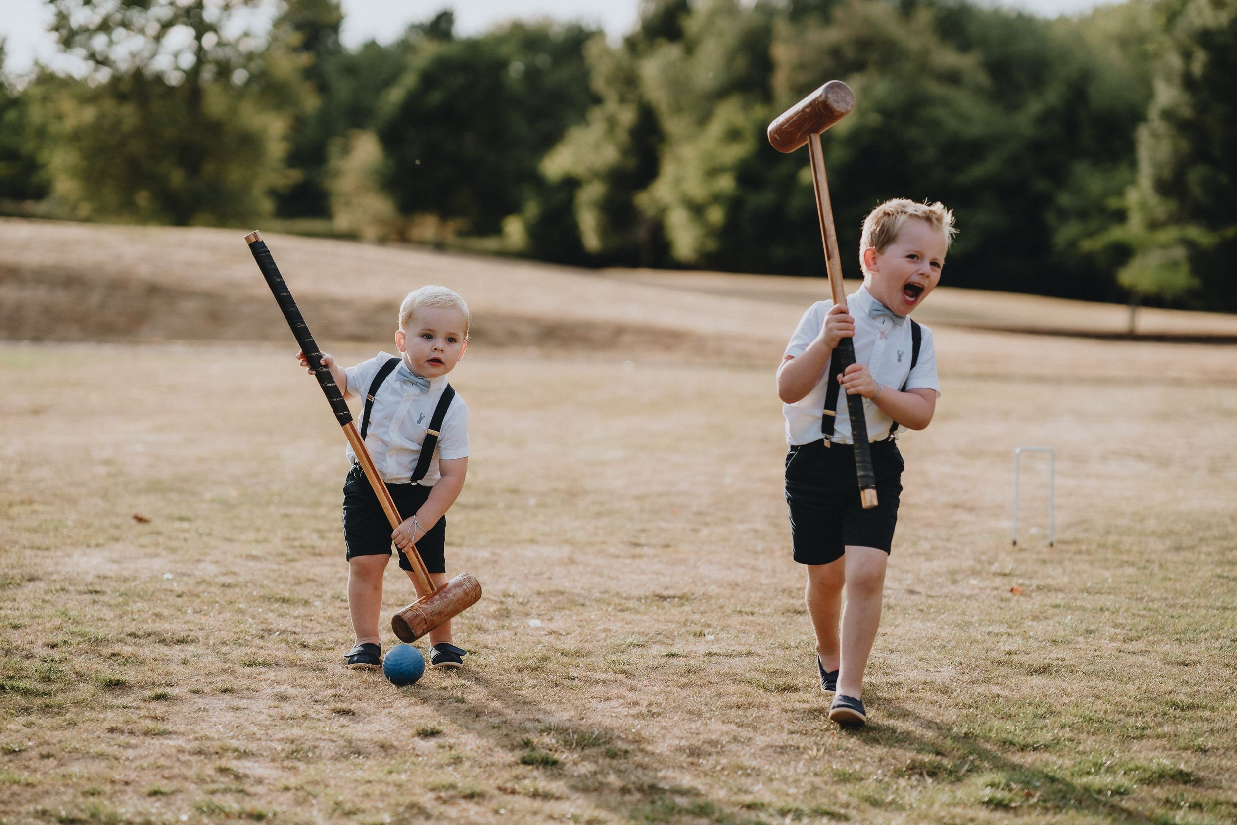 Two children in vintage style outfits play with old-fashioned tools in a sunlit field during summer.