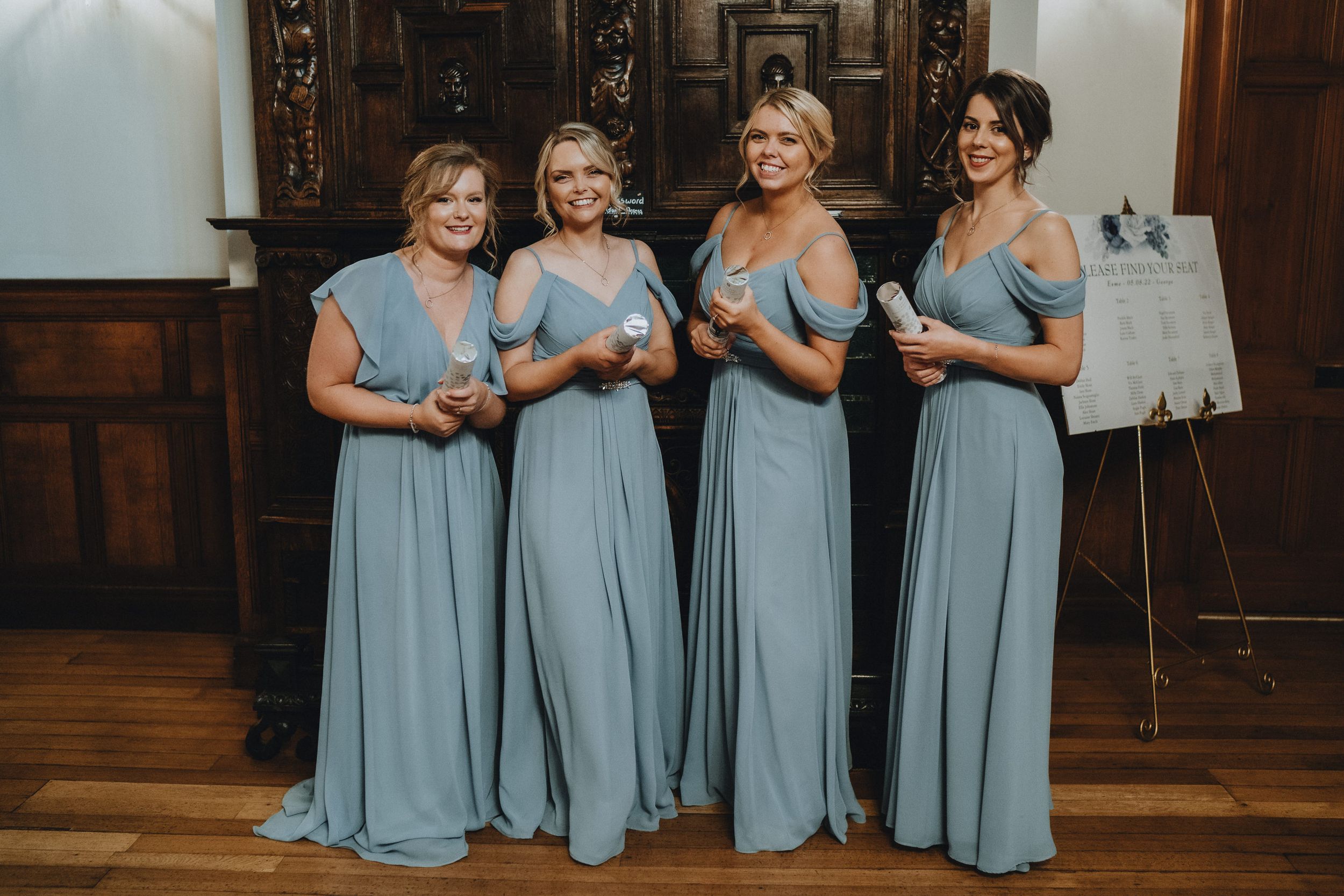 Four bridesmaids in matching powder blue floor-length gowns stand together in a wooden-paneled room.