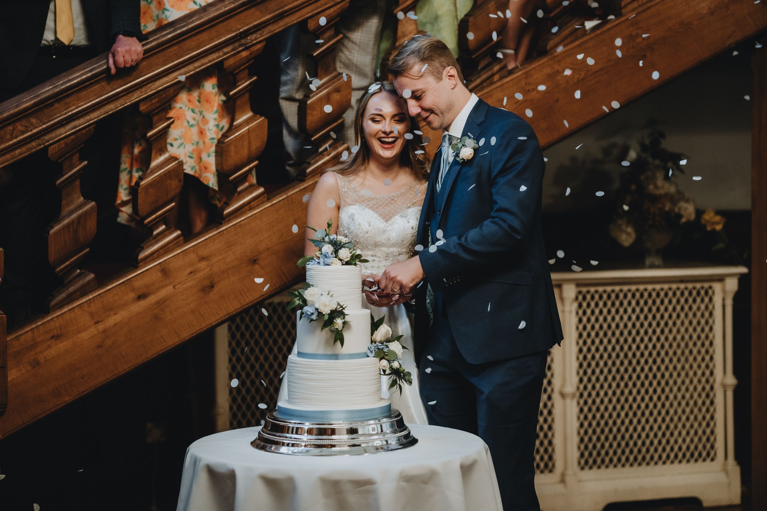 A wedding couple shares a joyful moment while cutting their semi-naked wedding cake in an elegantly decorated venue.