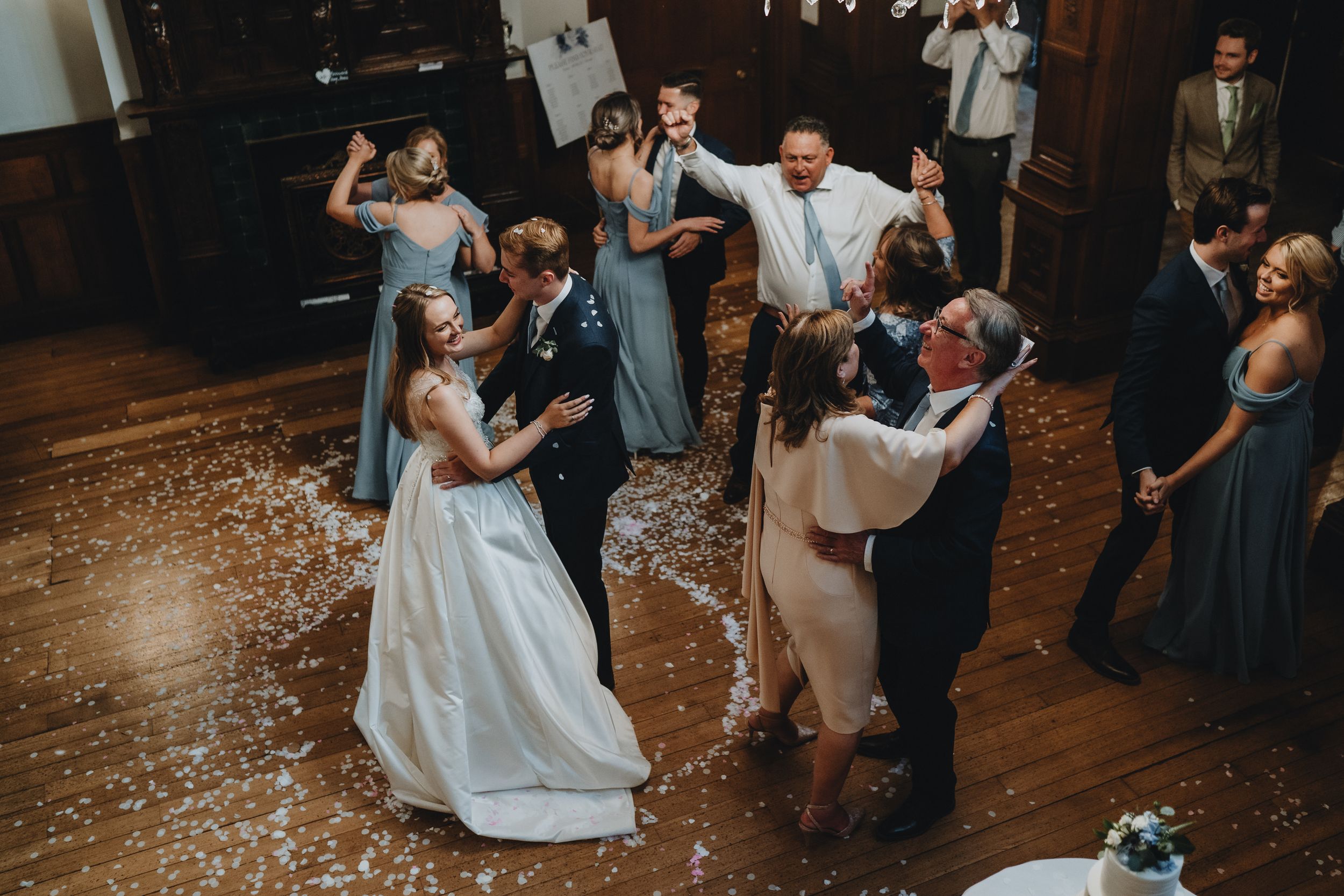 Guests enjoy dancing and celebrating at a wedding reception on a wood dance floor with flower petals scattered about.
