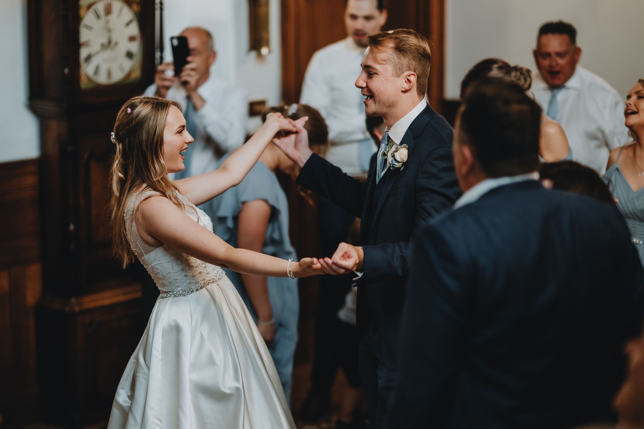 A couple dances together at their wedding reception in an indoor venue with a vintage clock on the wall.