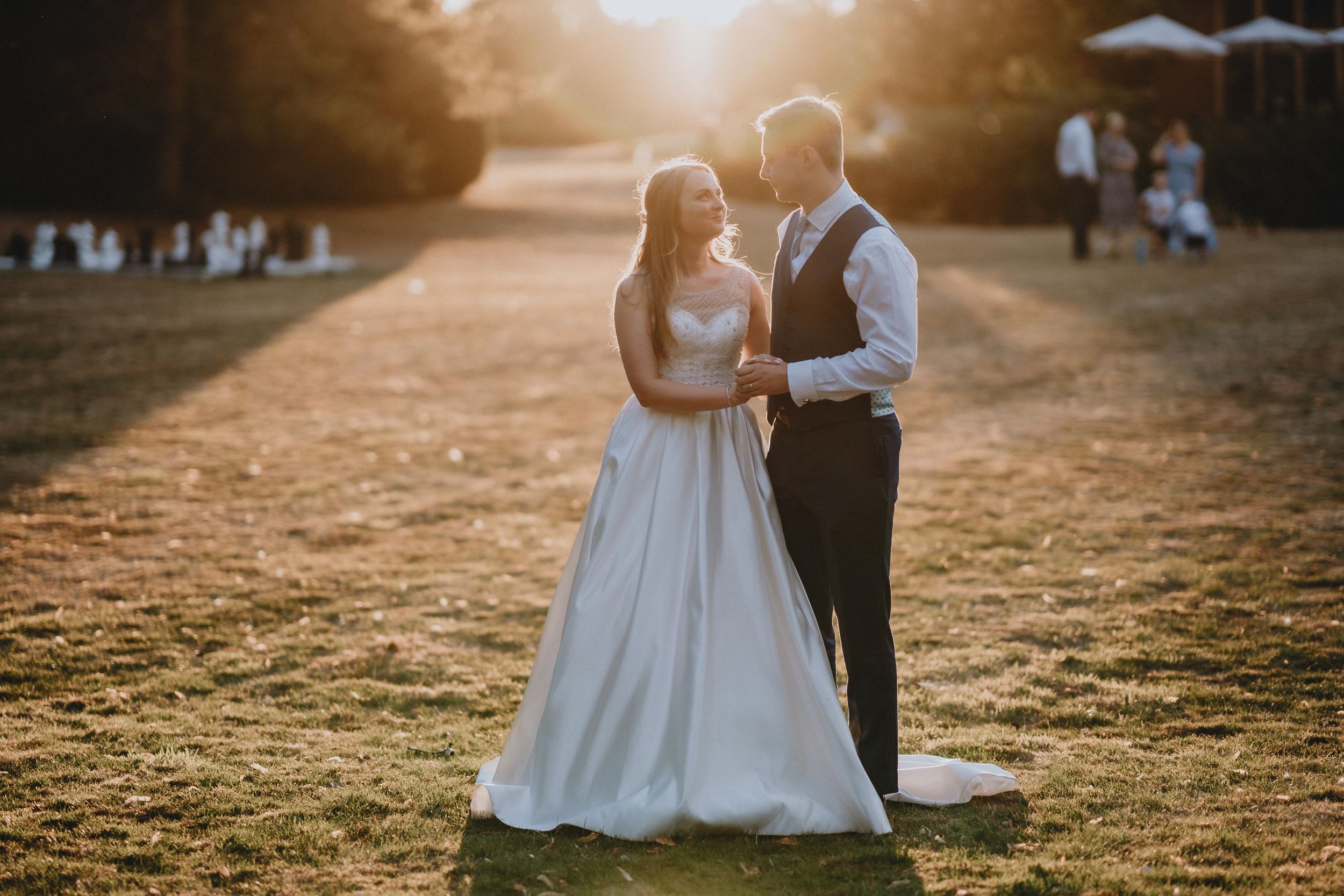 A couple shares a romantic moment at sunset in a grassy field during their wedding celebration at Holmewood Hall.
