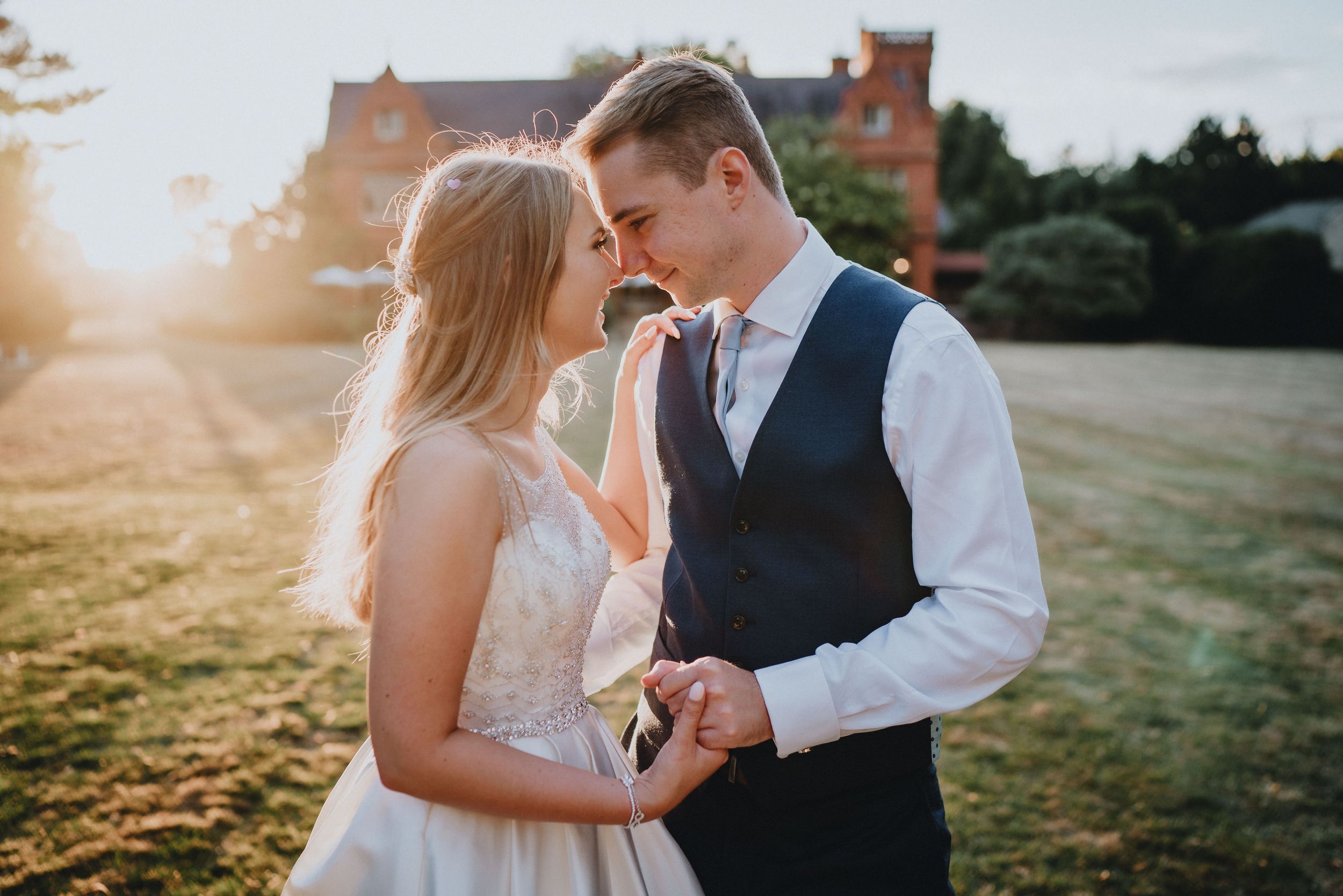 A couple shares an intimate moment at sunset on their wedding day at Holmewood Hall, with golden light illuminating the scene.