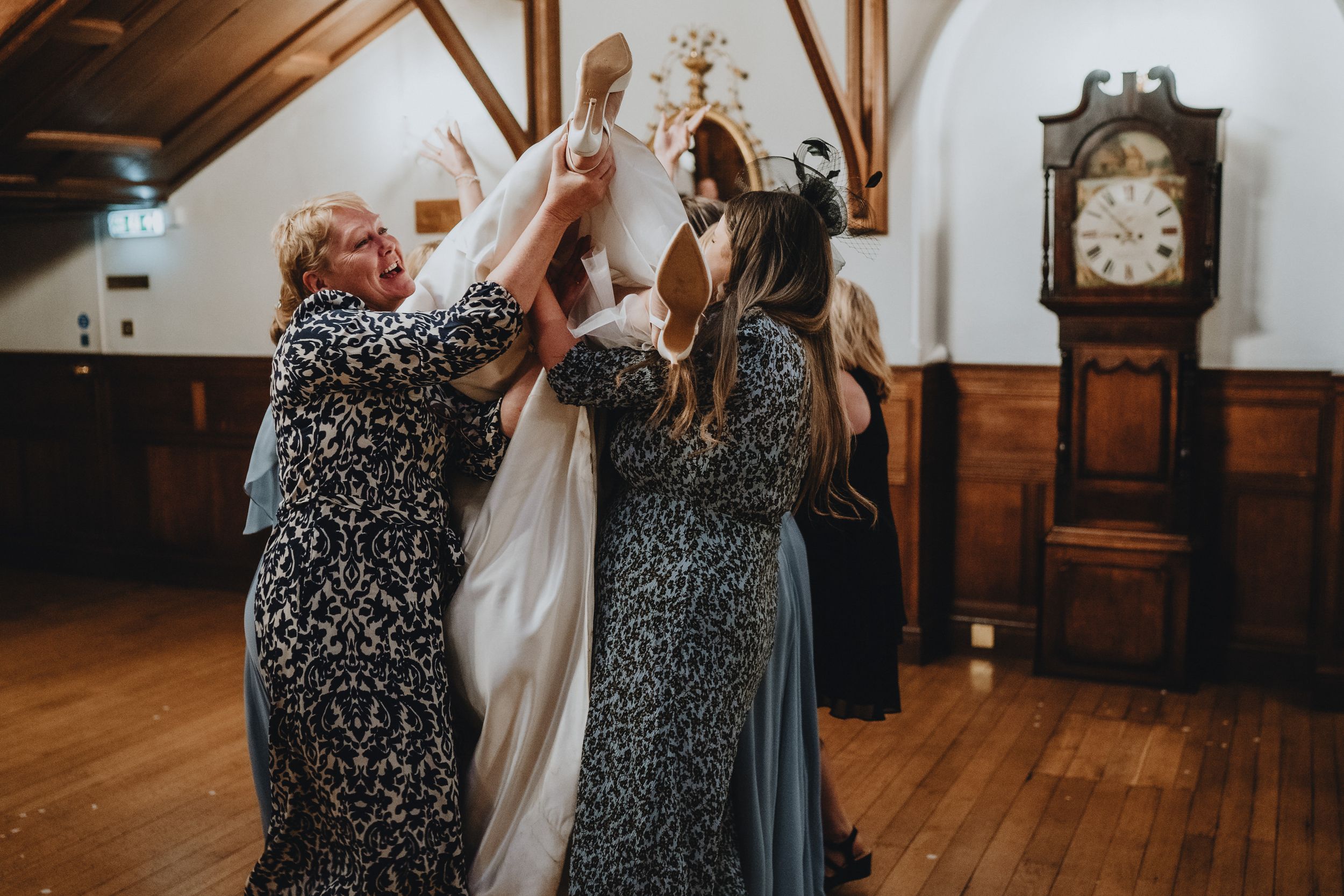 Two elegantly dressed guests in matching patterned dresses celebrate joyfully on a wooden dance floor at an event.