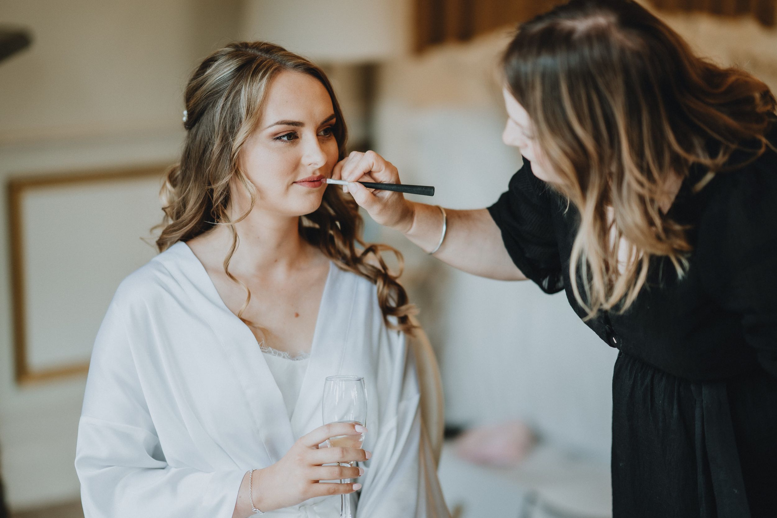 Makeup artist applying cosmetics to a client wearing a white robe during wedding preparations.