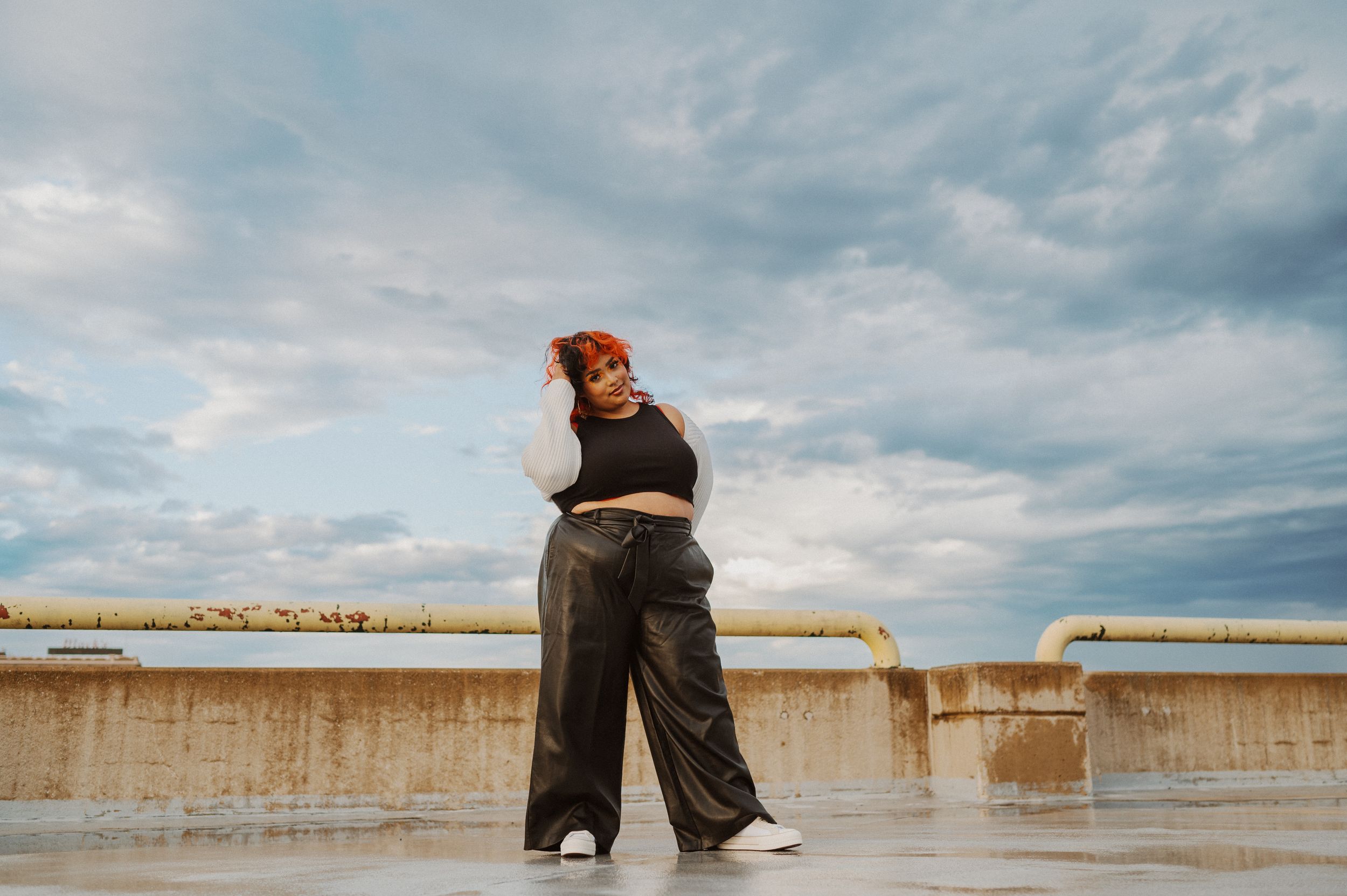 A figure in dark clothing walks along a concrete wall under cloudy skies in a minimalist landscape scene.