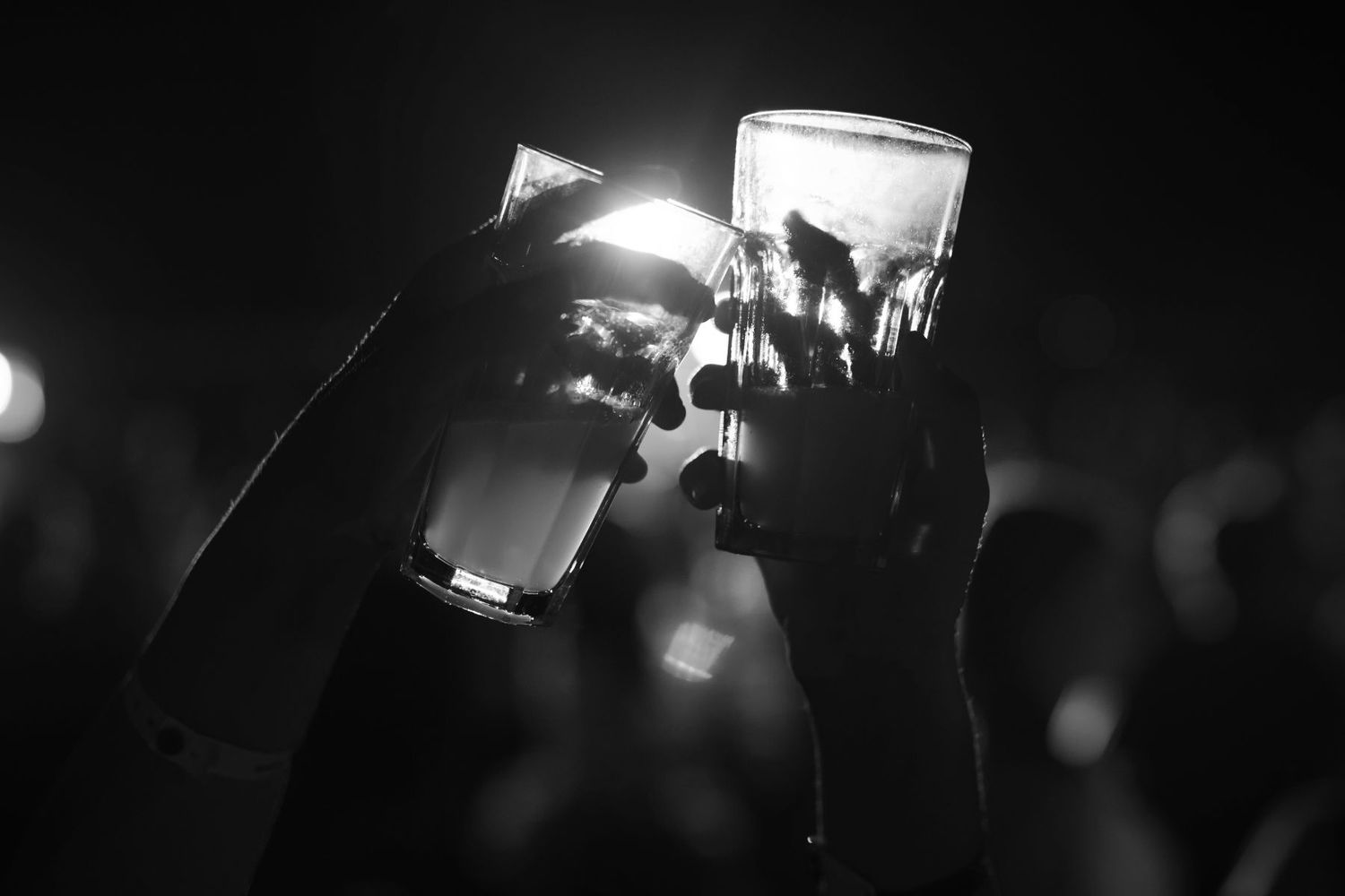 Silhouetted hands hold up glowing smartphone screens at a dark concert venue as lights twinkle in the background.