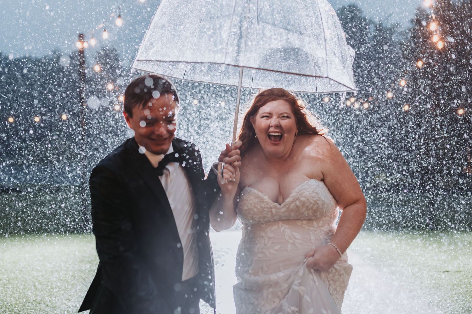 A couple embraces under an umbrella in the rain during what appears to be a wedding photo session.