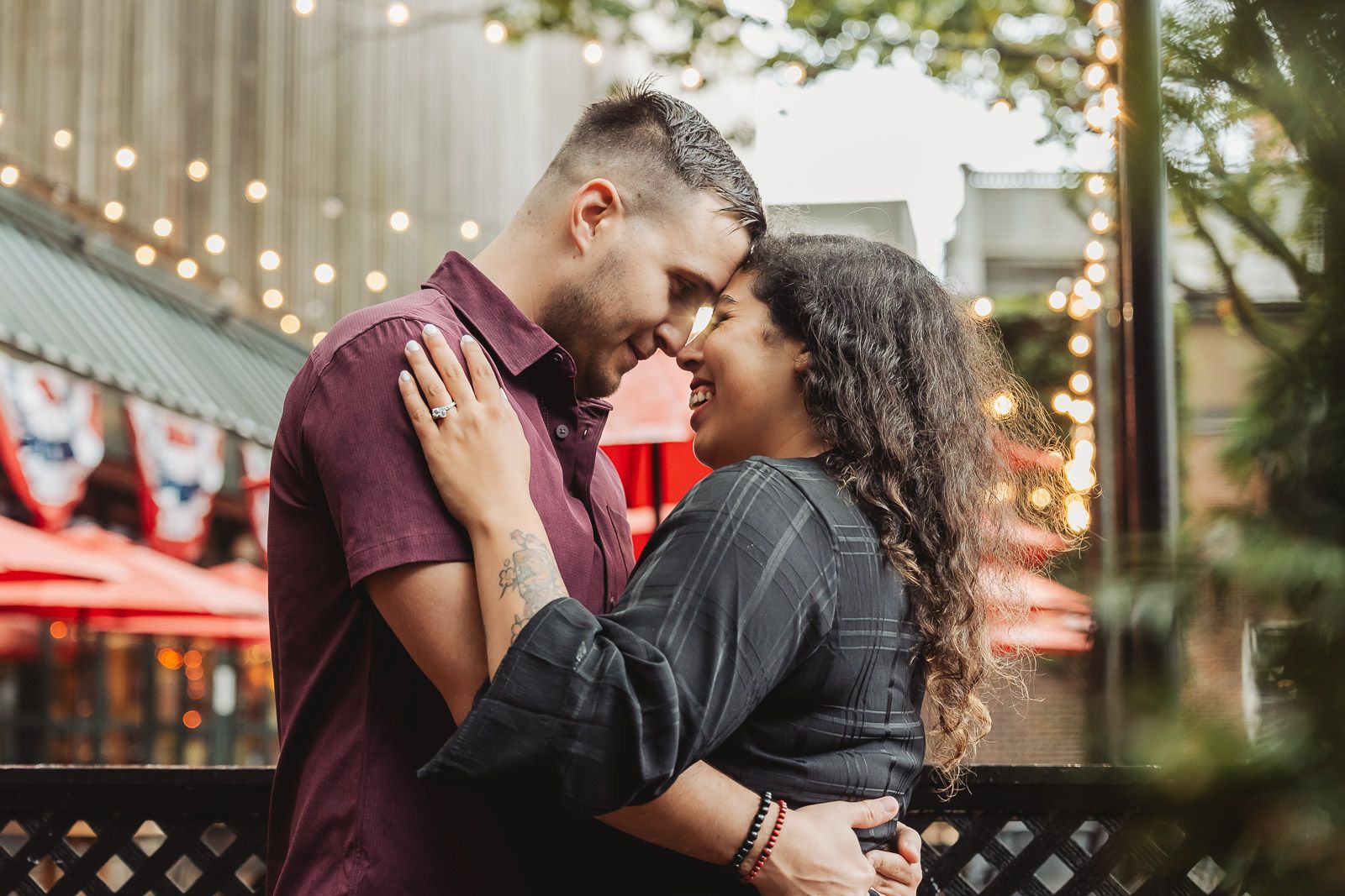 Tender moment between couple embracing against backdrop of string lights and red decor.