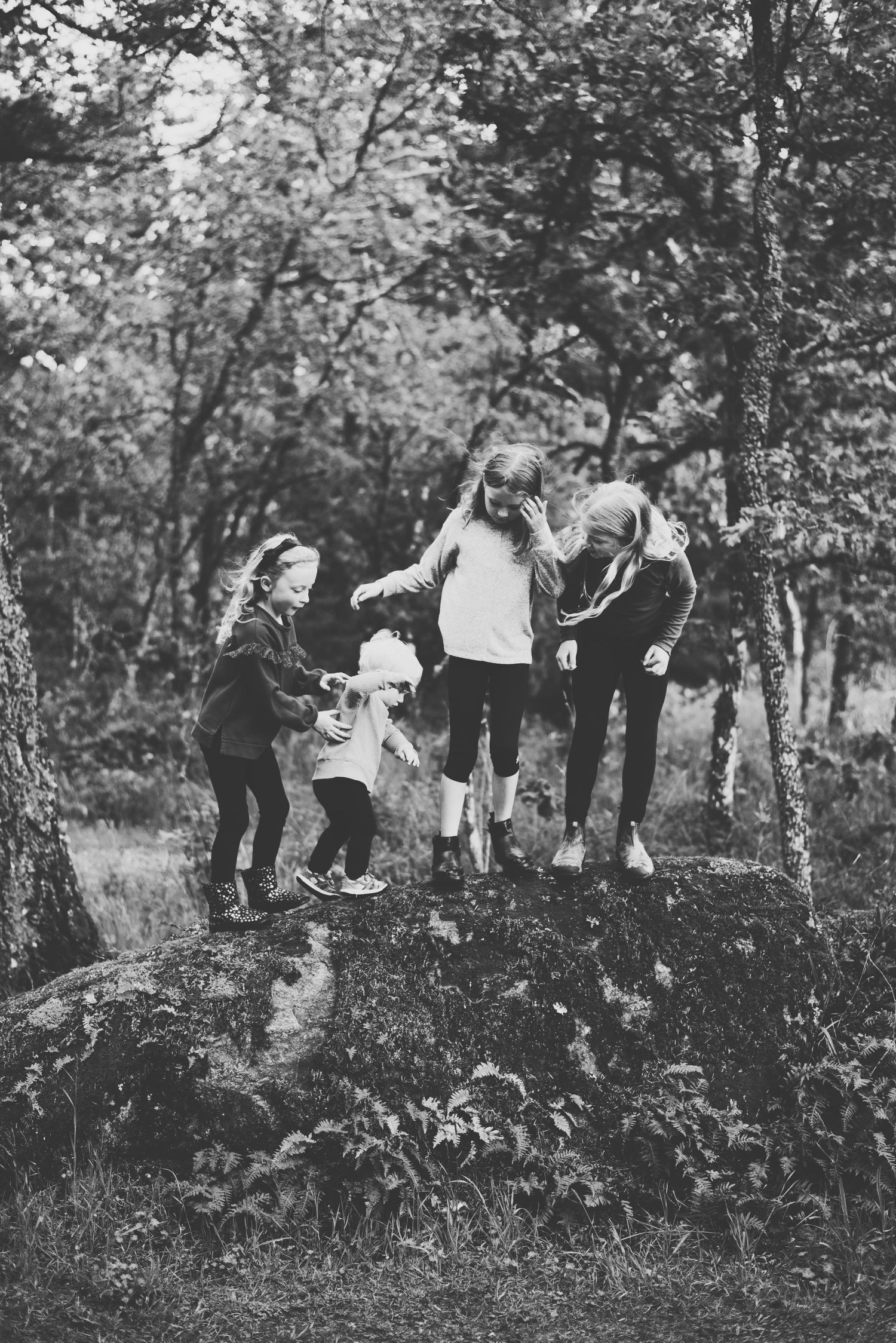Four children standing on a large rock in a forest, laughing and holding hands as they share a playful moment together.
