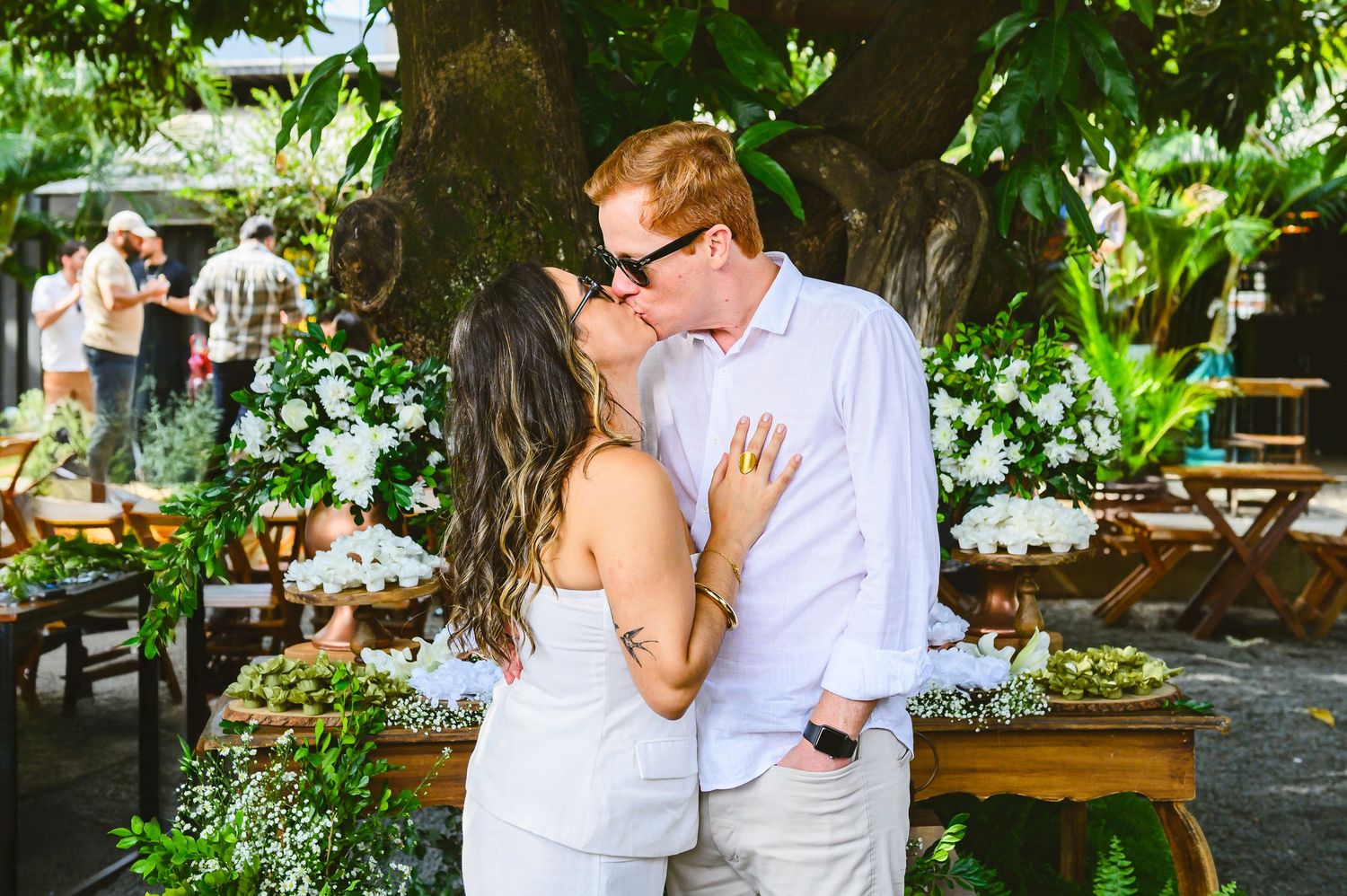 A romantic wedding couple shares an intimate moment under a lush green tree canopy during their outdoor garden celebration.