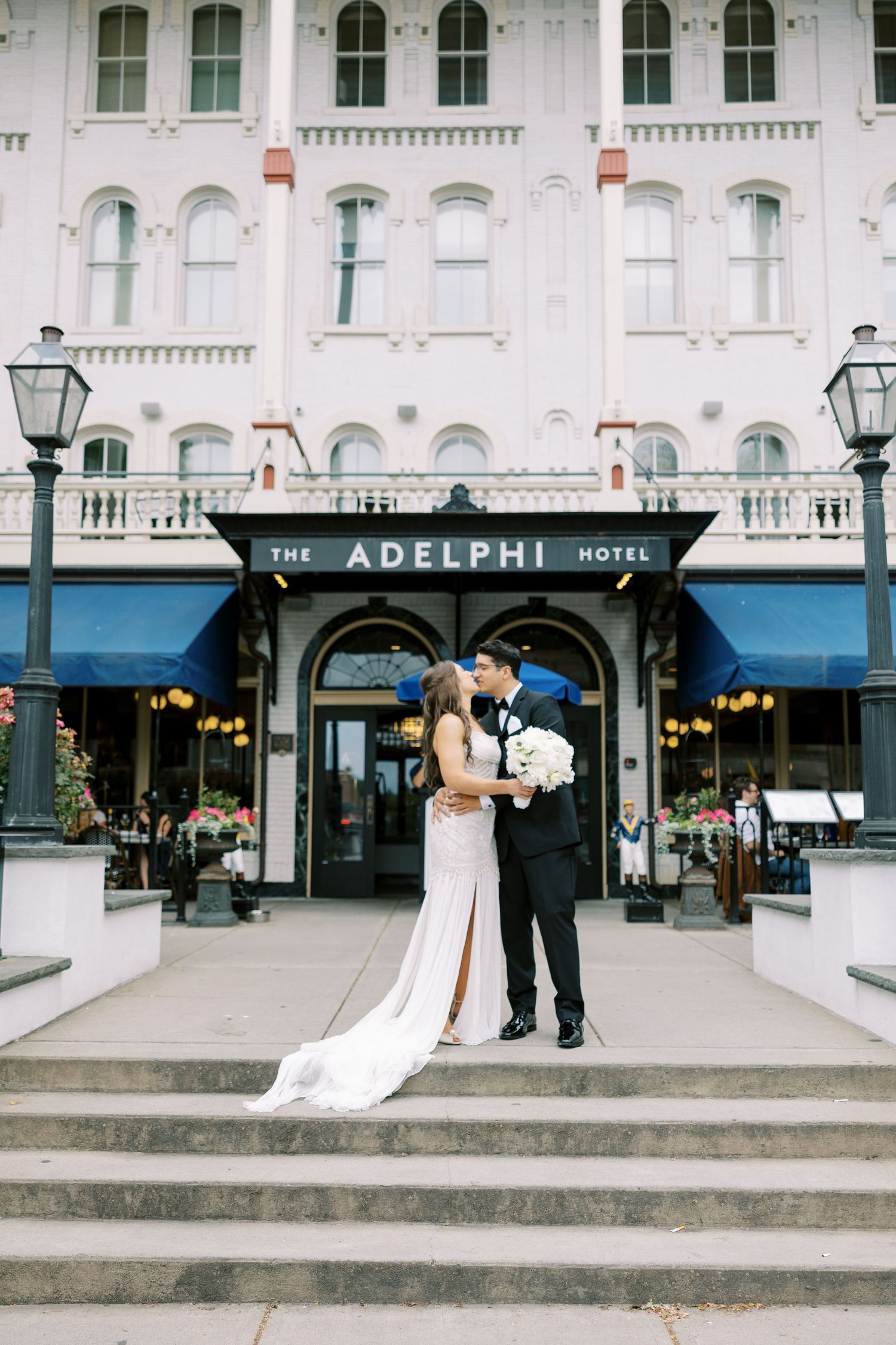 Wedding couple stands on the steps of the historic Adelphi Hotel building in what appears to be Liverpool.
