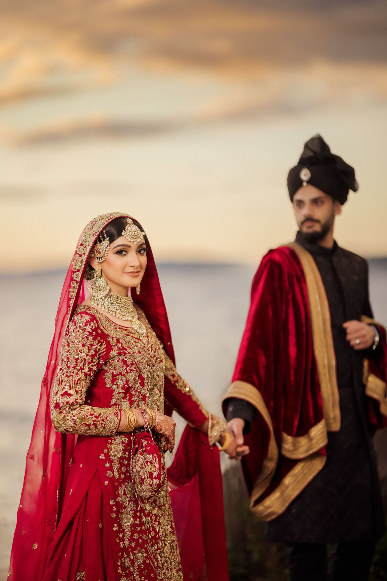 Elegant South Asian wedding scene with traditional red and gold attire photographed in a series against a sunset backdrop.