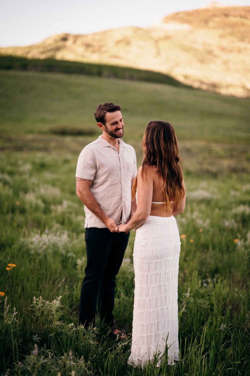 Couple sharing tender moment in mountain meadow with rolling hills in background.