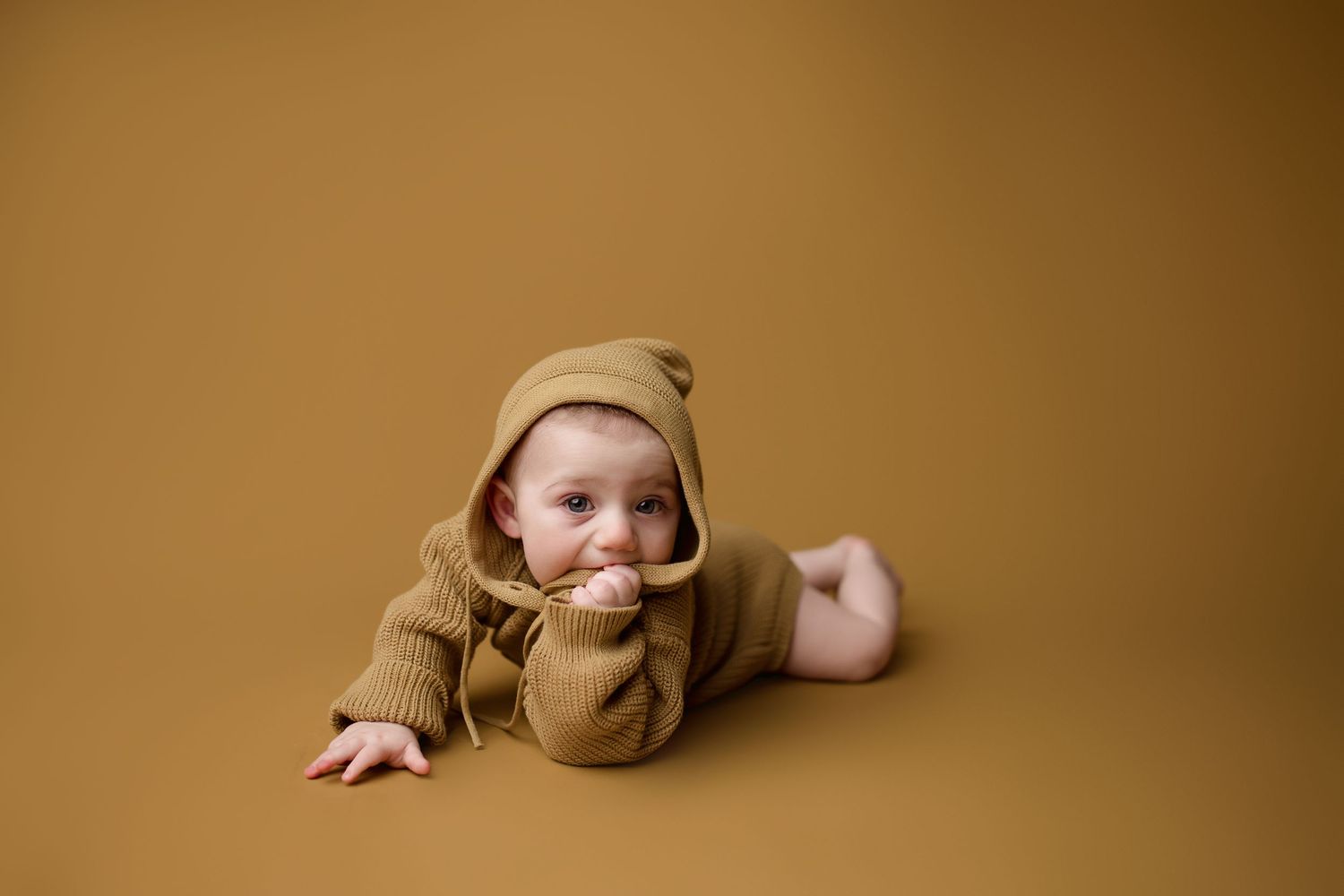 Baby wearing cozy brown knit outfit lies on brown backdrop during studio photography session.