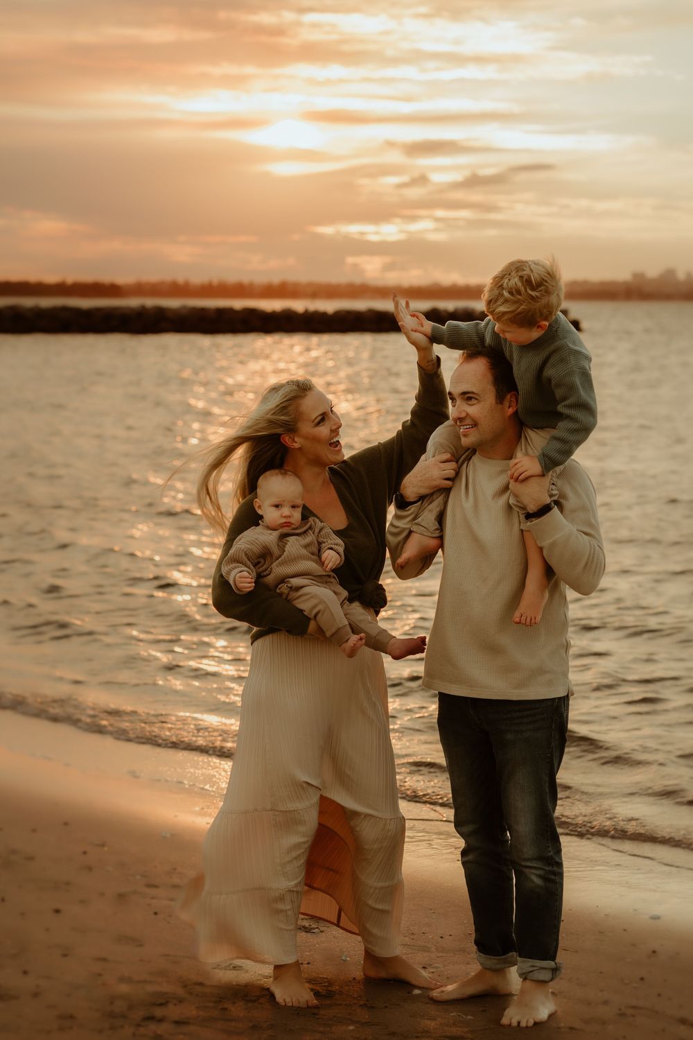 A family enjoys a joyful moment together while walking along the beach at sunset with golden light reflecting on the water.