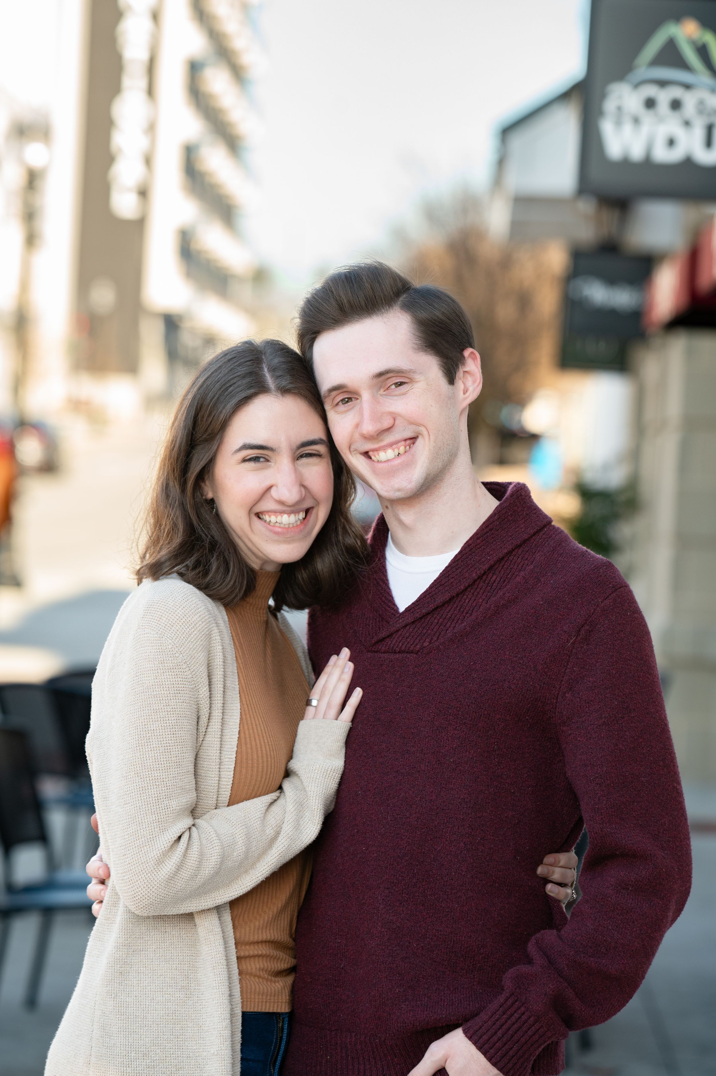 A happy couple embracing outdoors while wearing winter sweaters in front of a storefront.