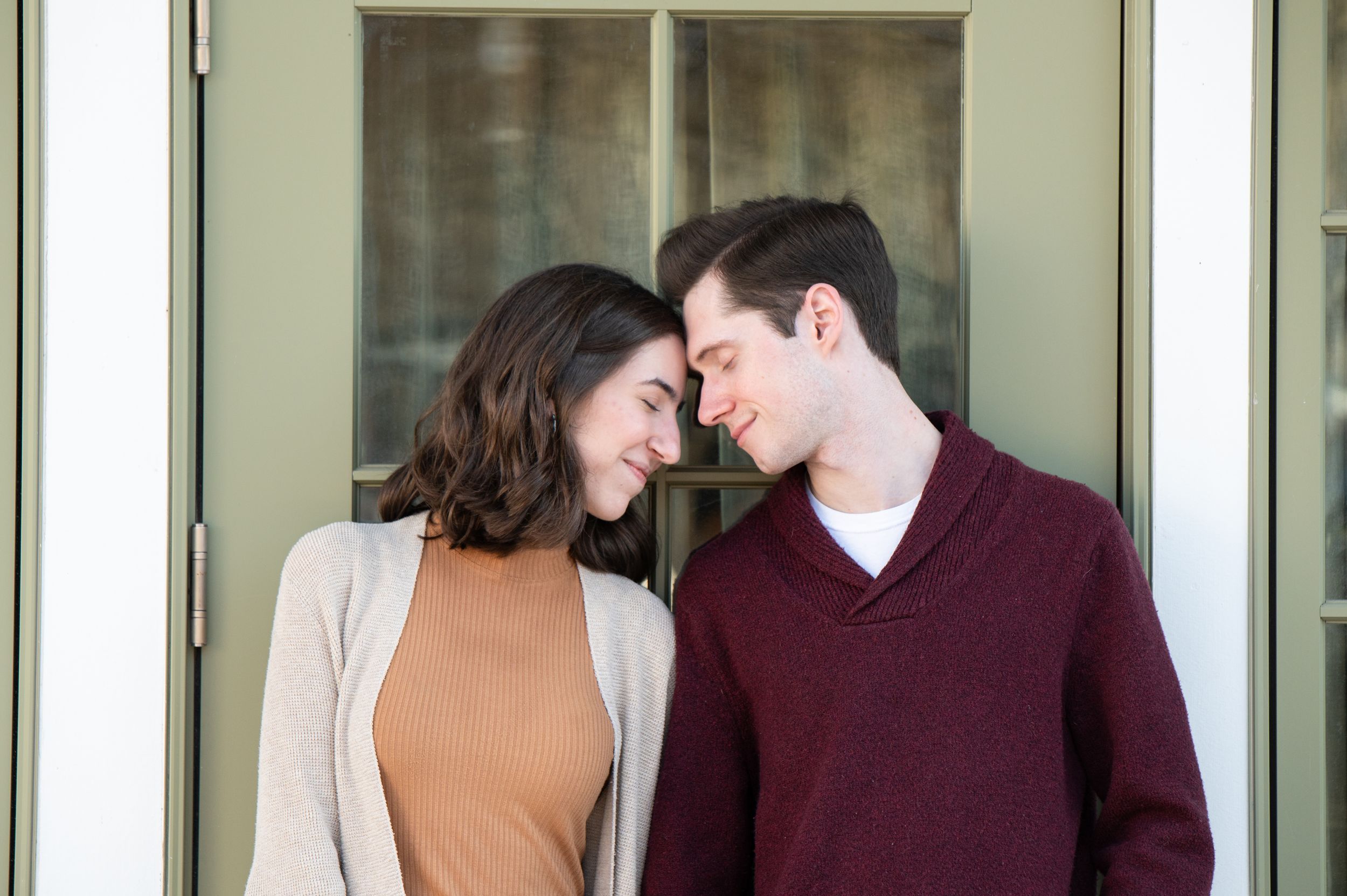 Couple sharing a tender moment together outside on sunny day wearing burgundy and tan sweaters.