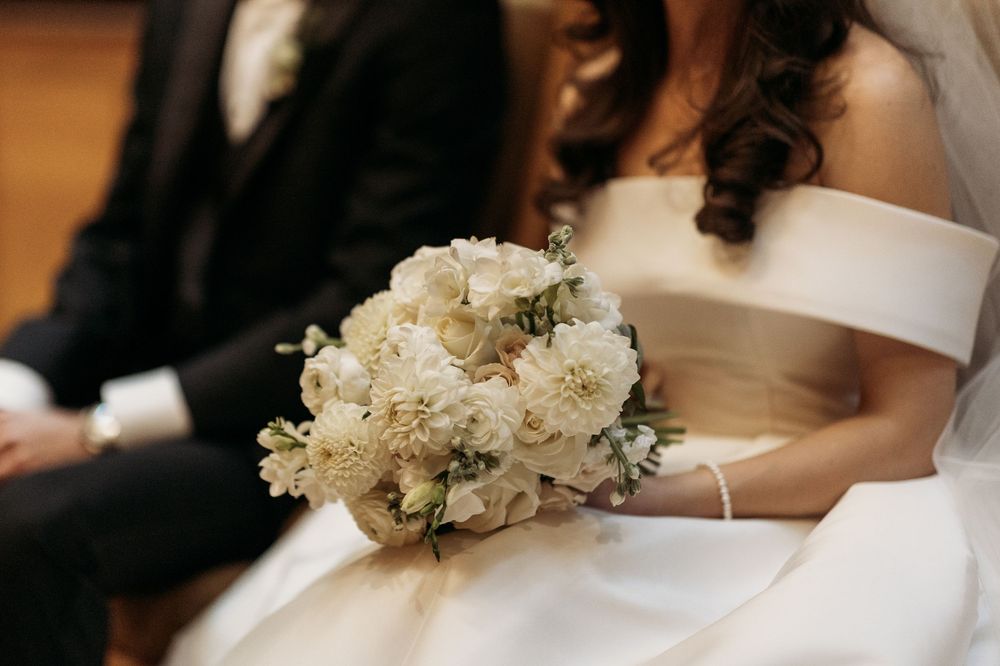 A delicate white and cream wedding bouquet rests against an elegant off-shoulder wedding gown.