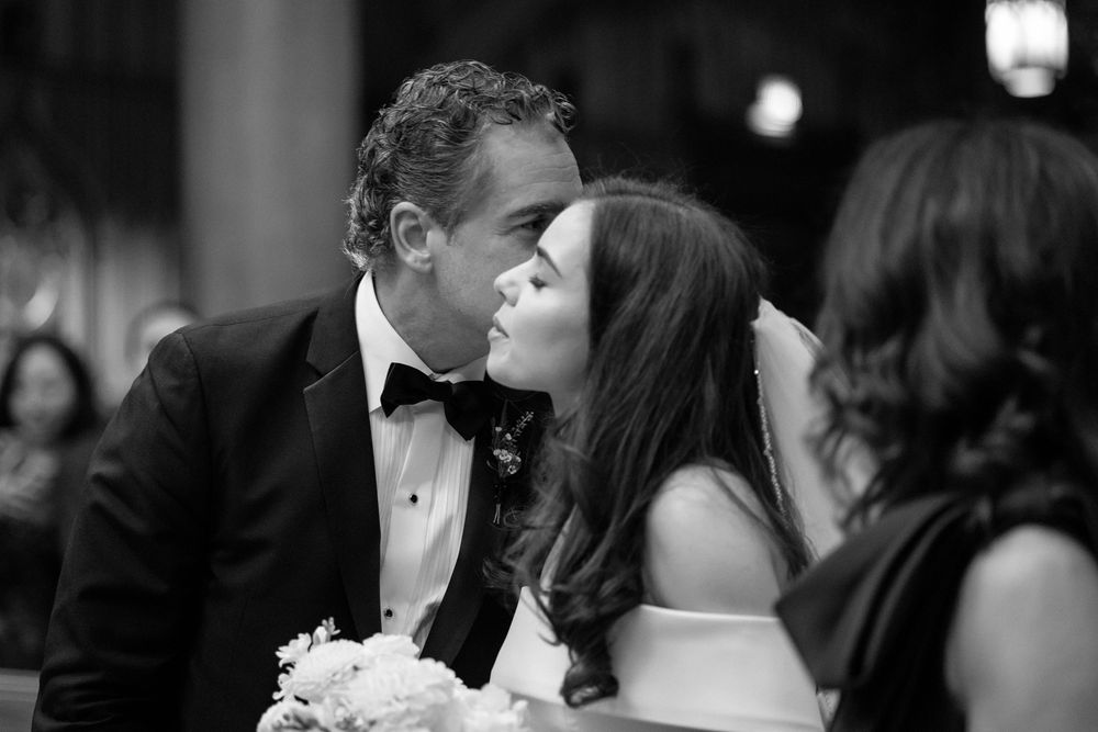 A romantic black and white candid moment between a couple in formal attire sharing a tender kiss at an elegant event.