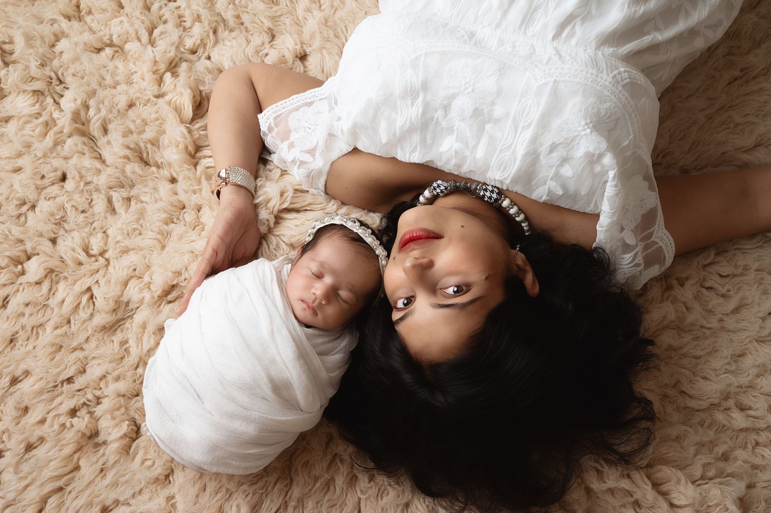 Mother and baby lying on beige carpet in artistic overhead portrait.