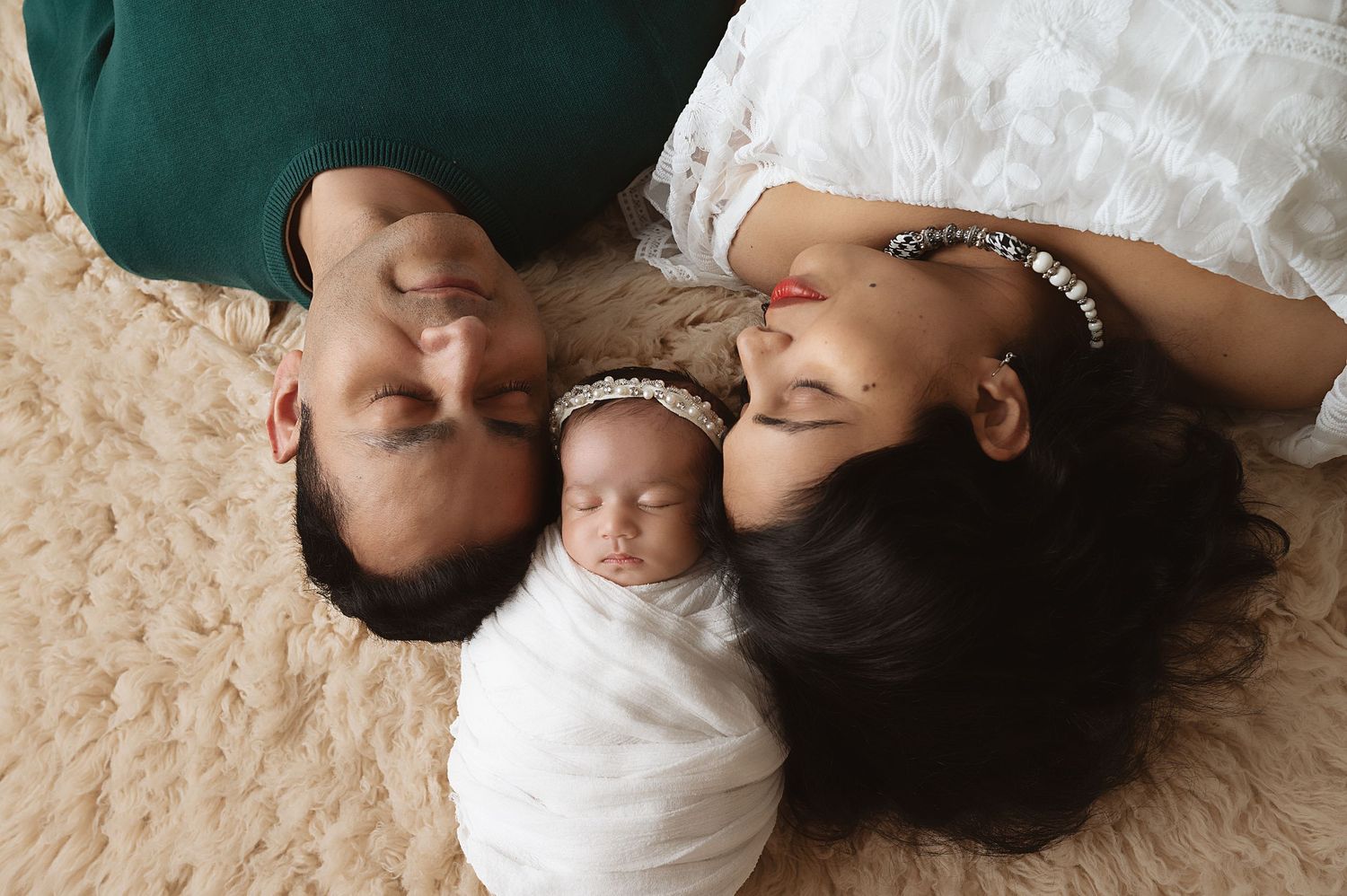 Family lying on beige carpet with swaddled baby in heartwarming portrait.