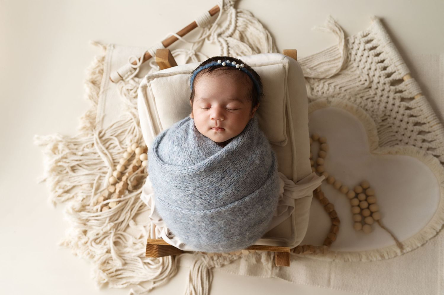 Newborn baby wrapped in soft gray swaddle sleeping peacefully in decorative wooden crate with macrame details.