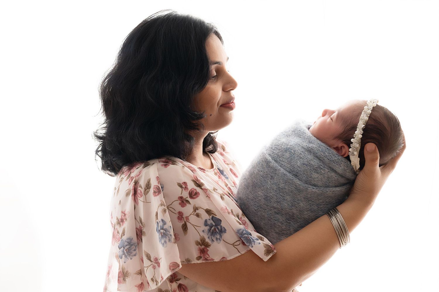 Mother in floral dress holding swaddled newborn baby in gentle pose.