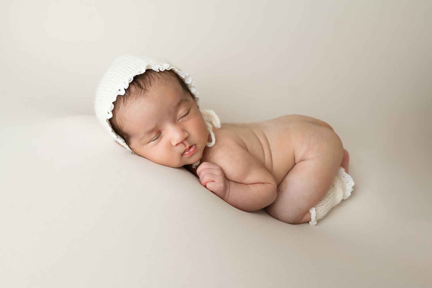 Sleeping newborn wearing white headband posed on neutral background during photo session.