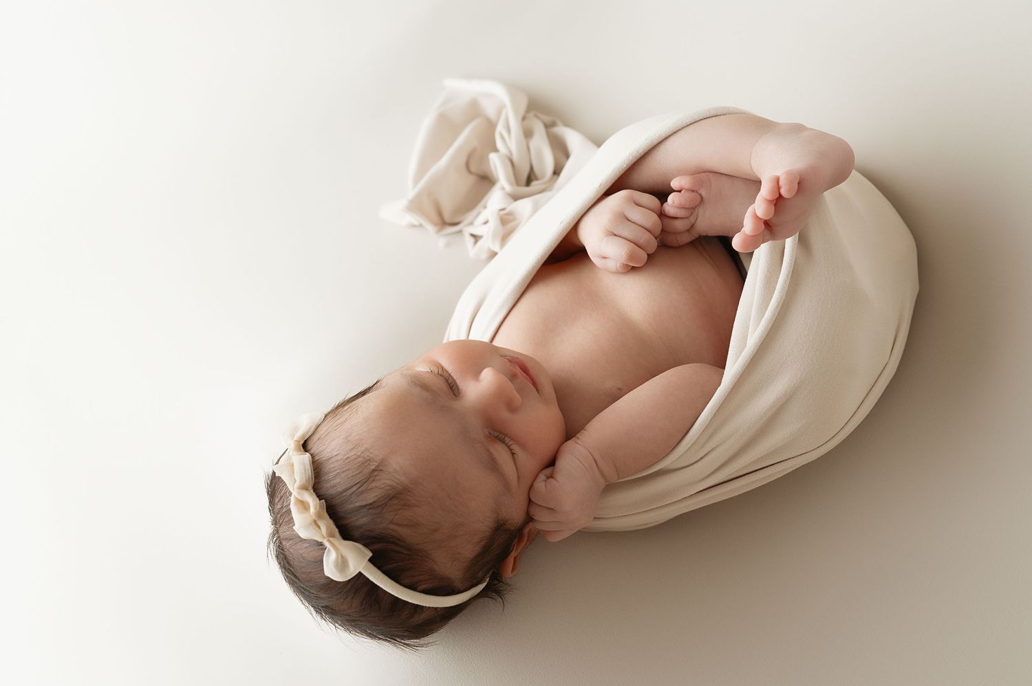 Overhead view of sleeping newborn baby wrapped in cream fabric during studio session.