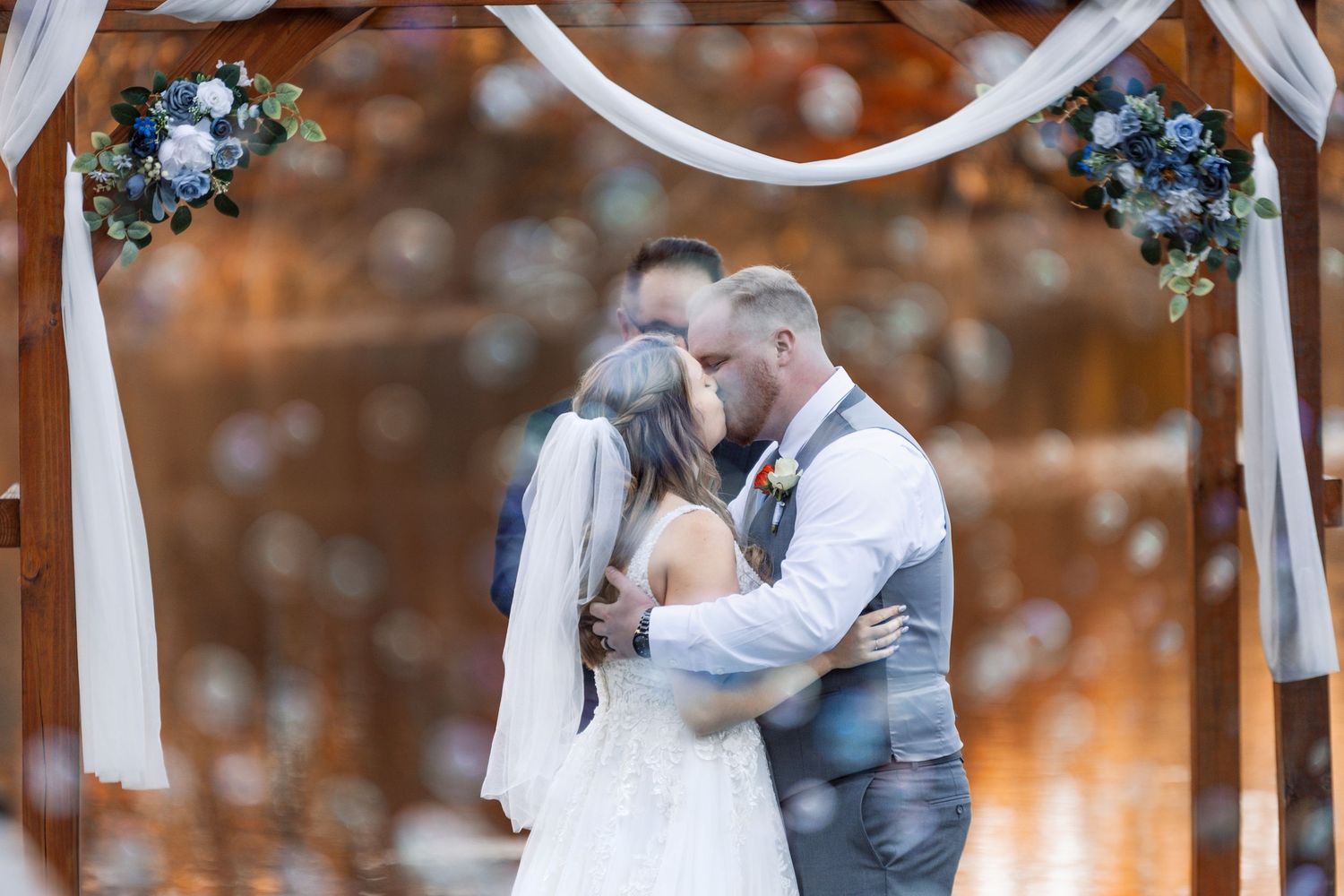 A beautiful outdoor autumn wedding scene showing a young flower girl in a white dress holding a bouquet of flowers.
