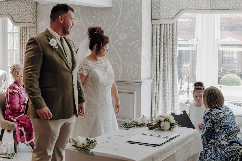 Wedding ceremony at a bright indoor venue with elegant decor and white floral arrangements.