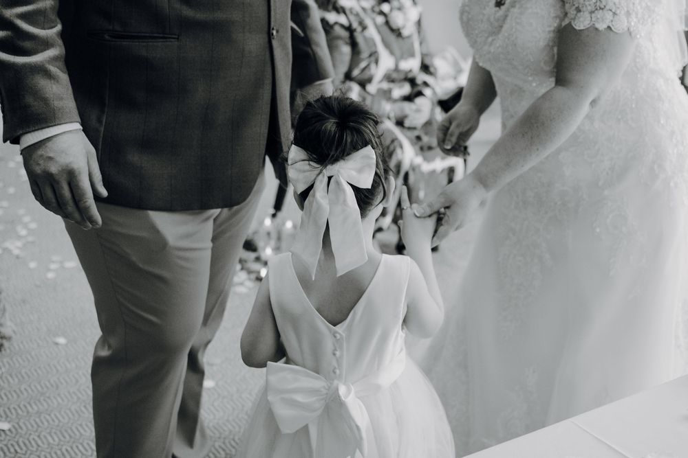 Black and white shot capturing an emotional moment between a small flower girl and a bride at a wedding ceremony.
