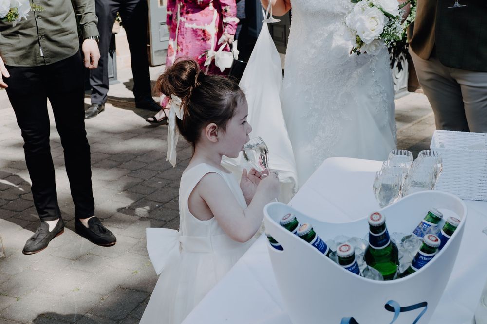People gather around a drinks cooler filled with beverages during an outdoor wedding celebration.