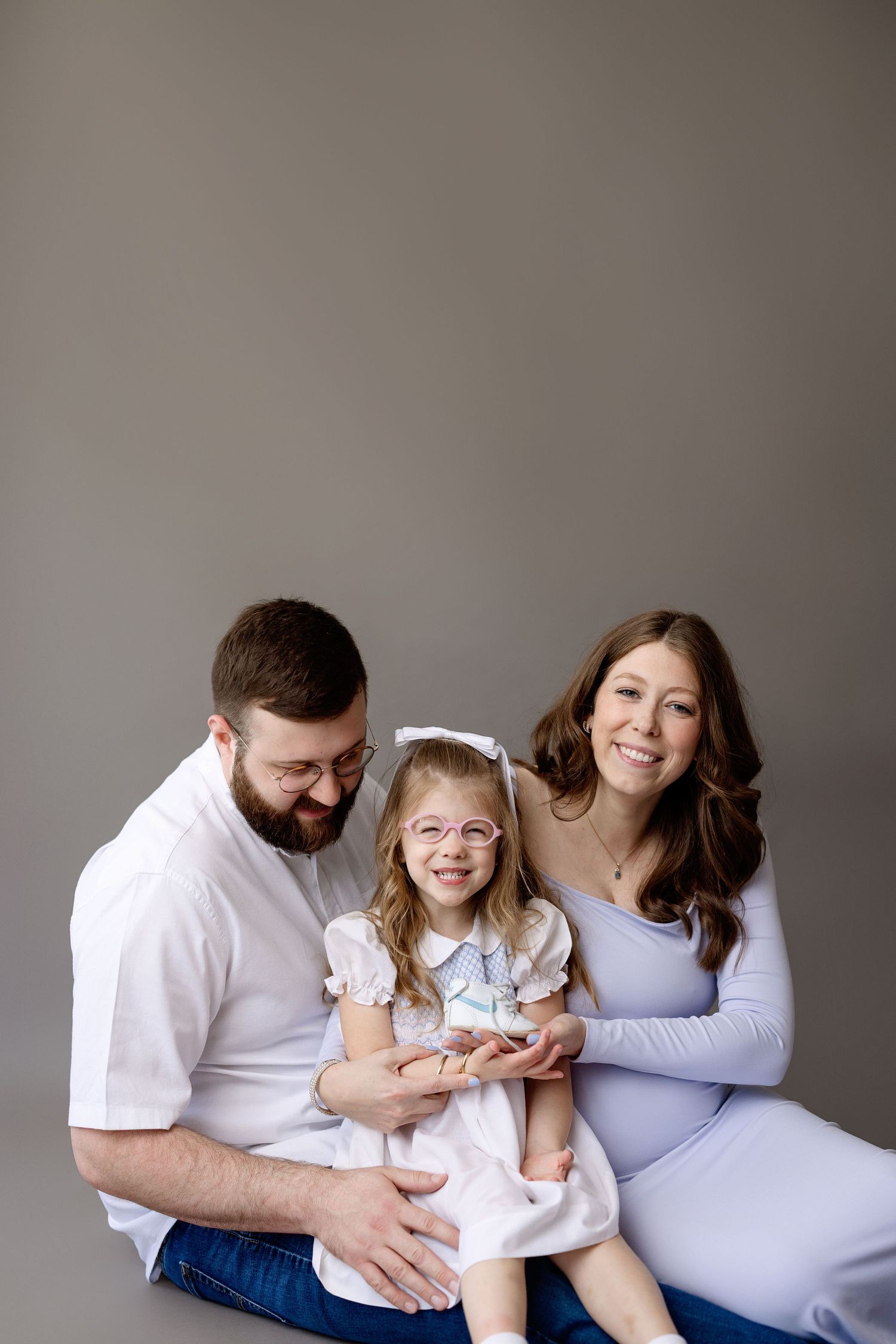 Happy family wearing white and light blue outfits pose together against neutral gray background.
