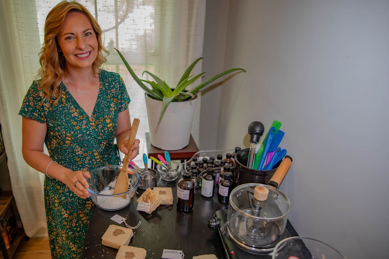 A person in a green floral dress measures ingredients while making homemade beauty products at a DIY workspace.