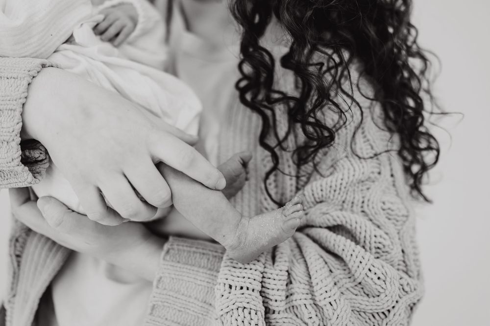 Close-up black and white image showing curly dark hair and a knit sweater while holding an infant.
